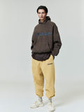 Full body view of model wearing brown Heavy Fleece 90s Hoodie with blue text and beige pants gallery 0 file 0000_HO25_F_L60_P33_2829.jpg