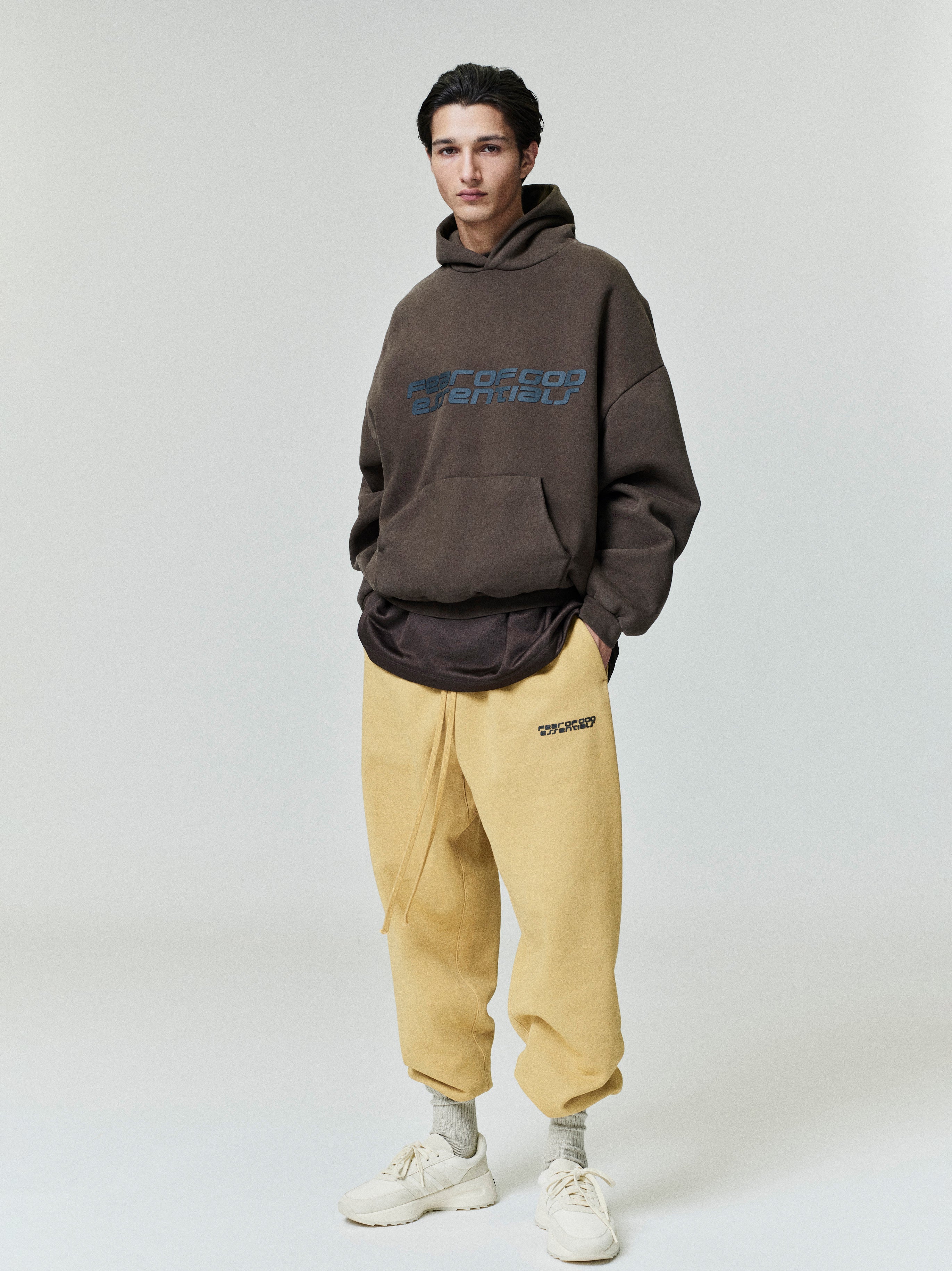 Full body view of model wearing brown Heavy Fleece 90s Hoodie with blue text and beige pants gallery 0 file 0000_HO25_F_L60_P33_2829.jpg