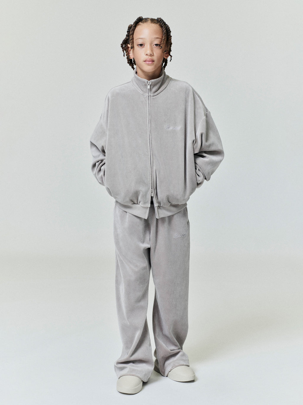 Child wearing light gray velour zip-up jacket and matching wide-leg velour sweatpants standing with hands in pockets