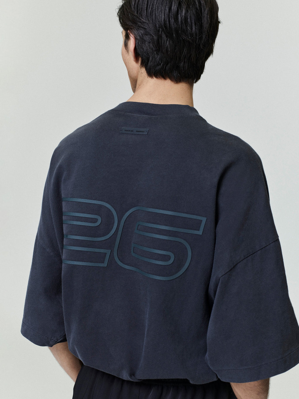 Person wearing a black teeshirt with '26' printed on the back against a plain background
