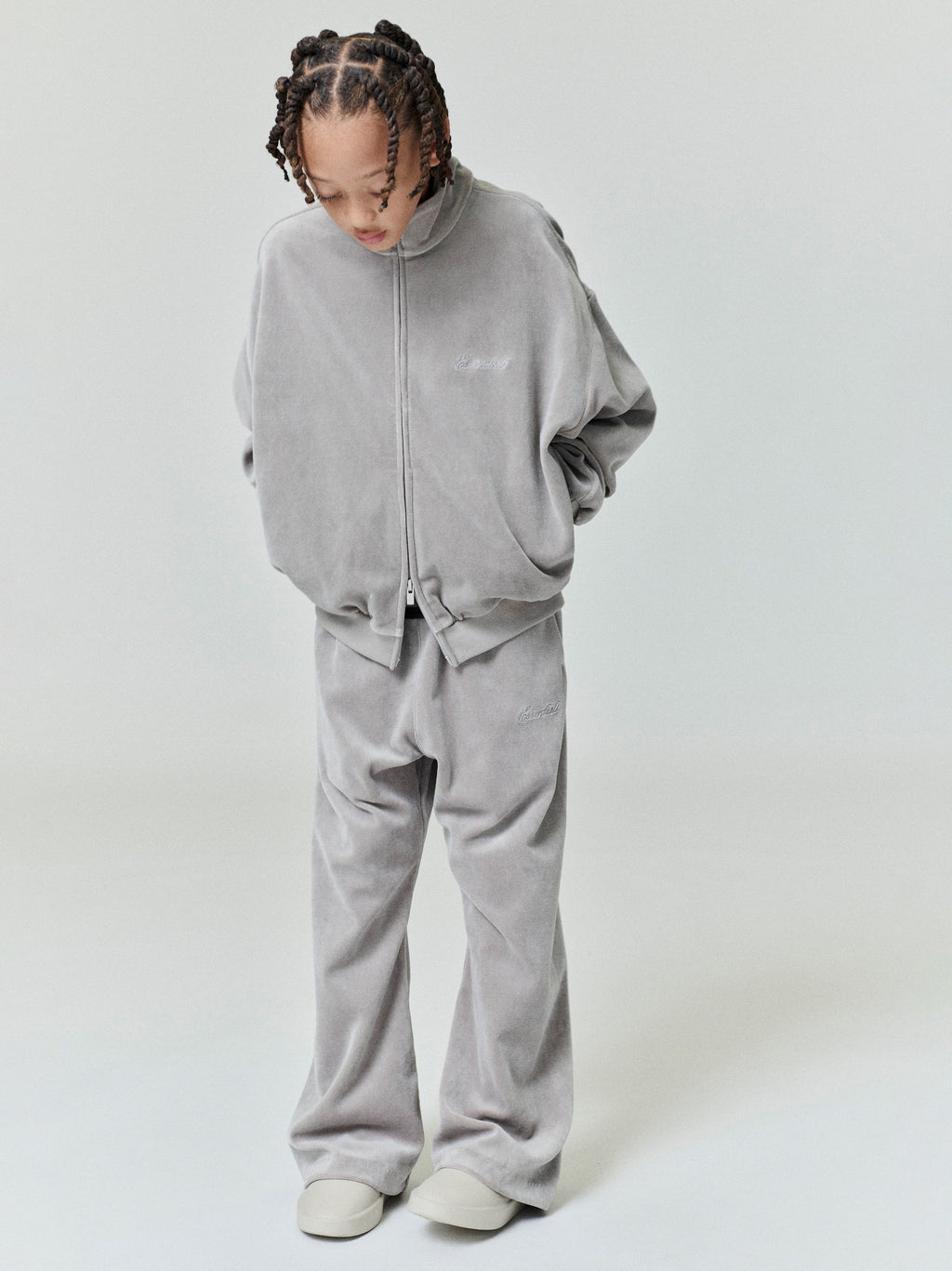 Child wearing gray velour zip-up jacket and matching wide-leg flare sweatpants looking downward against light background