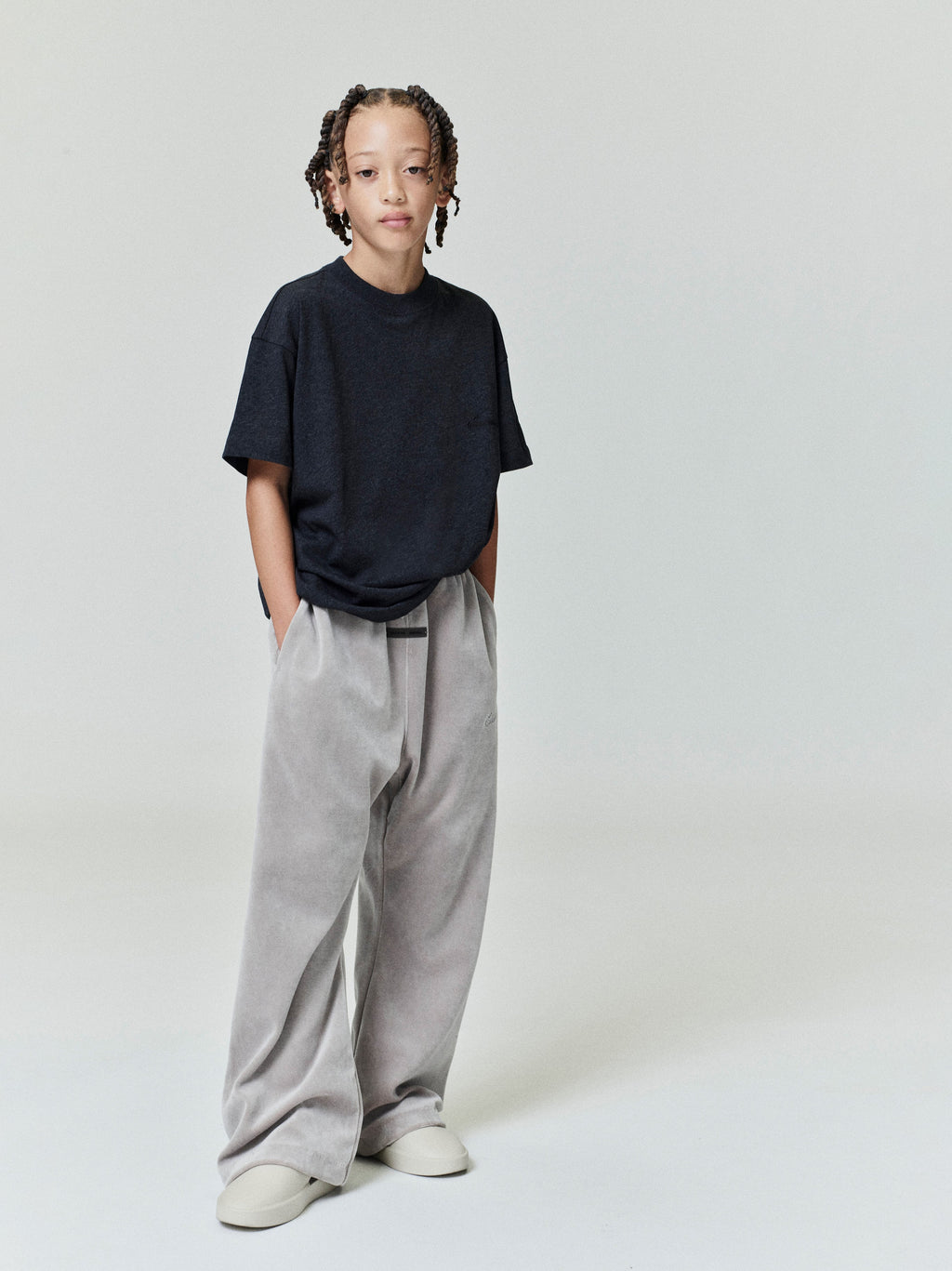 Full body view of child wearing black Kids Embroidered Essential Tee with relaxed fit, hands in pockets, gallery position 0