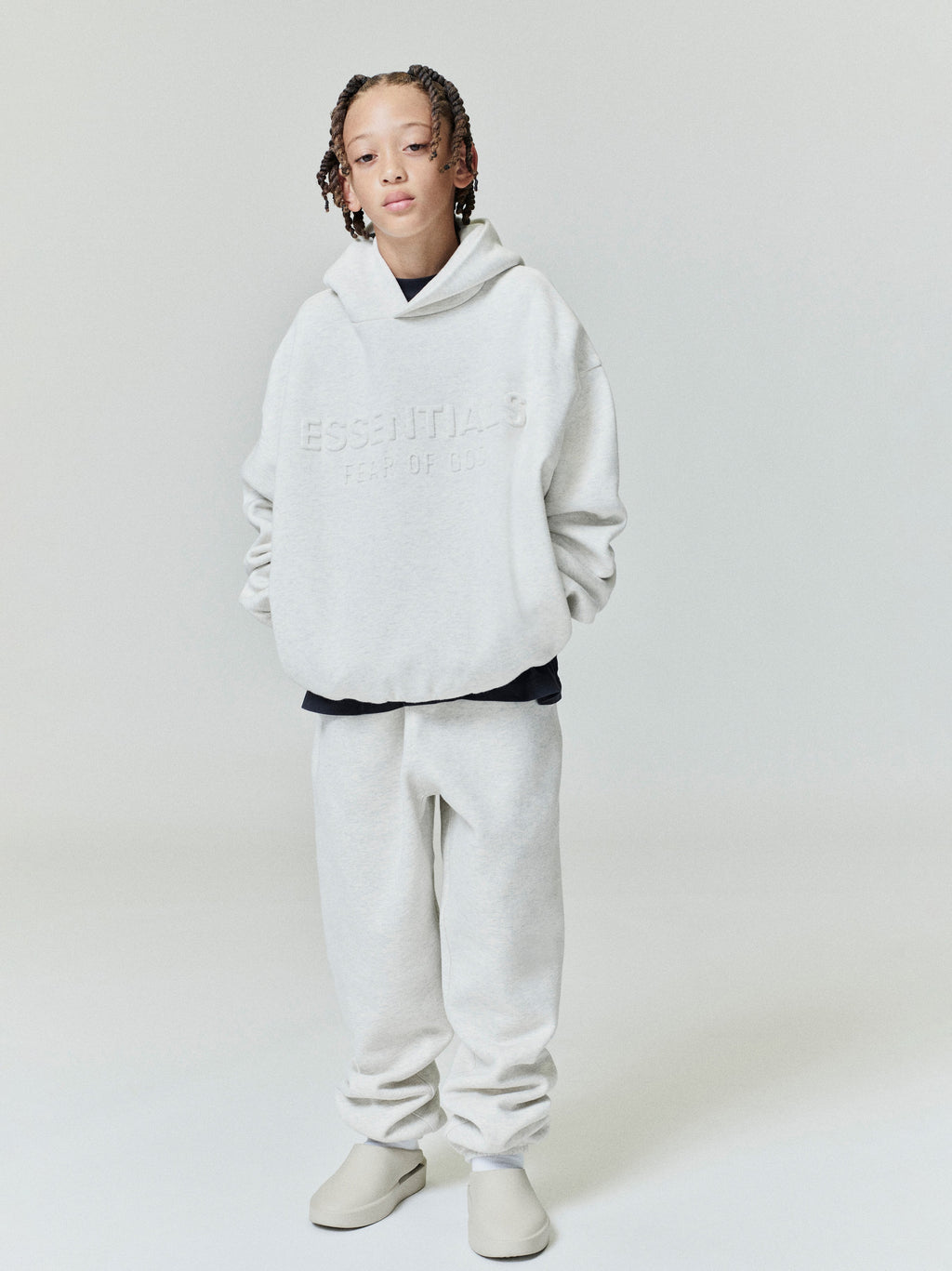 Full front view of oatmeal Kids Embossed Classic Hoodie with subtle raised ESSENTIALS text, gallery position 0, file 0004_HO25_K_L76_4035.jpg