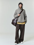Full-length image of model wearing grey Heavy Waffle 90s Hoodie with hood up and oversized fit holding a dark leather shoulder bag