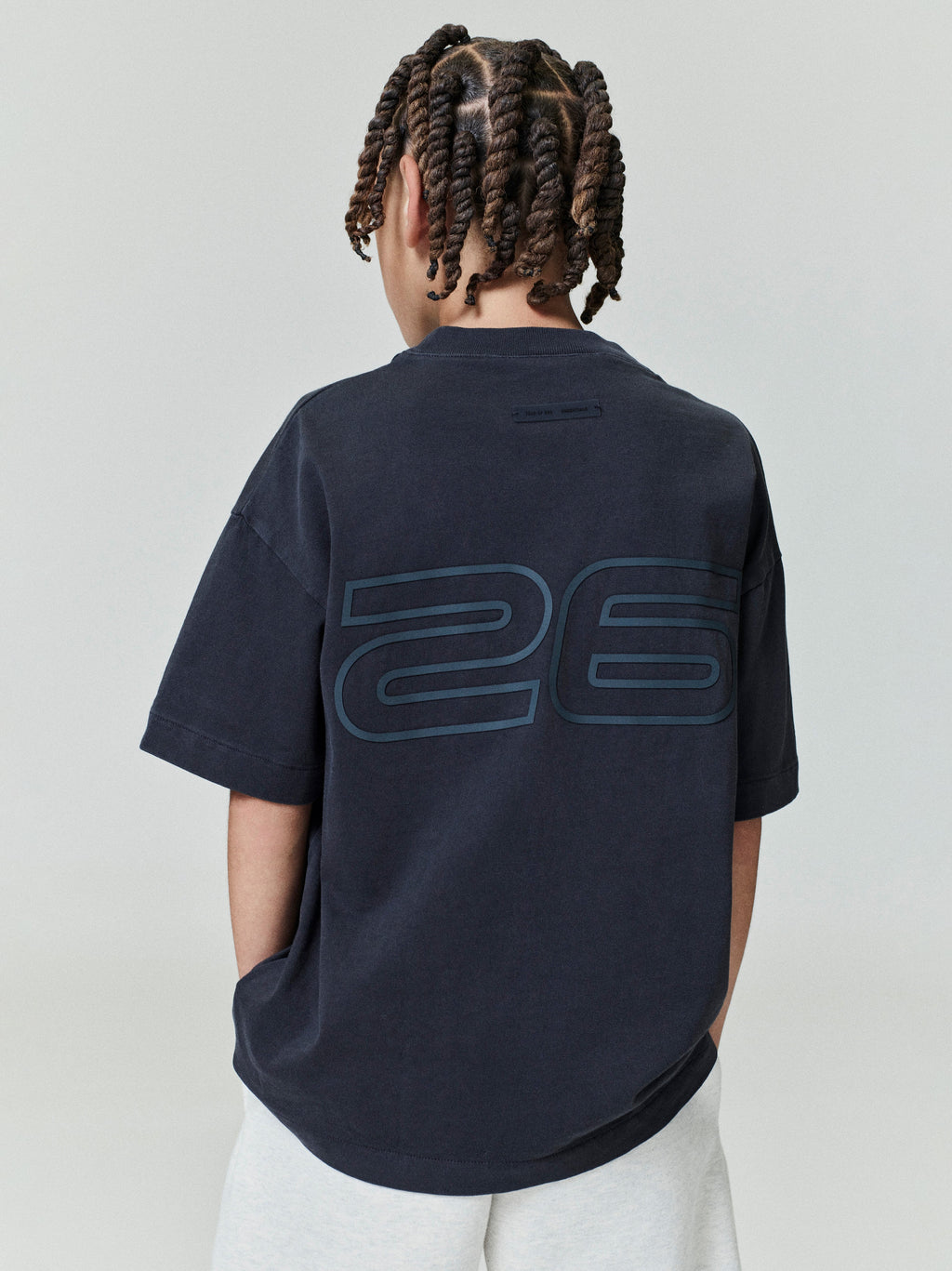 Back view of child wearing navy Kids Classic Short Sleeve Tee with large outlined "26" graphic, gallery position 0, file 0006_HO25_K_L75_4017.jpg