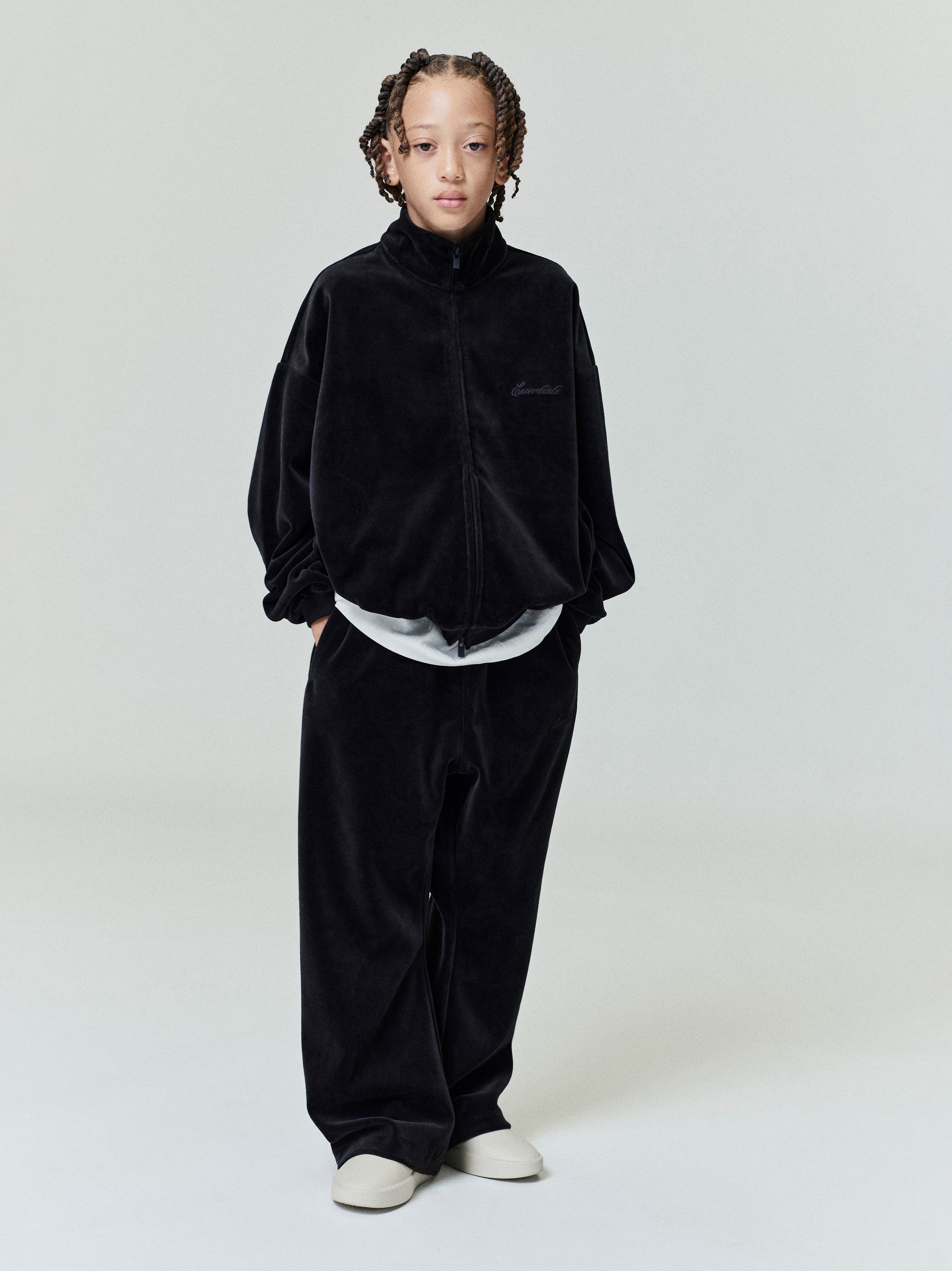 Child wearing a black velour zip-up jacket and matching wide-leg flare sweatpants standing with hands in pockets
