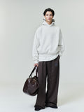 Model wearing oatmeal Embossed Essentials Classic Hoodie standing with hand in pocket and holding dark brown leather bag, studio shot