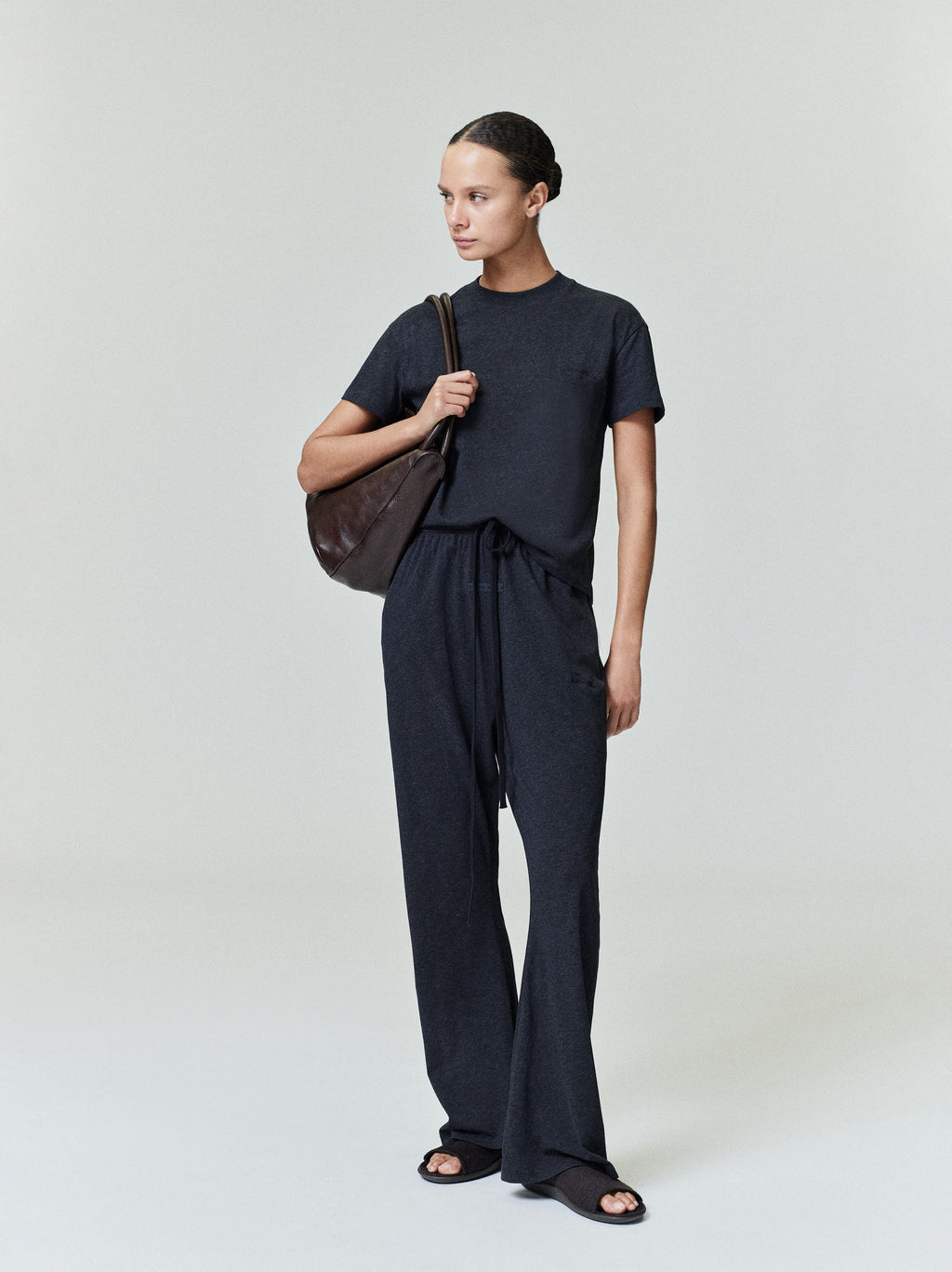 Full-length view of woman wearing vintage black Womens Embroidered Classic Tee standing with brown bag on neutral background