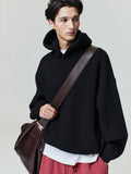 Male model wearing black Heavy Waffle 90s Hoodie with textured knit, oversized fit, and brown leather shoulder bag on neutral backdrop