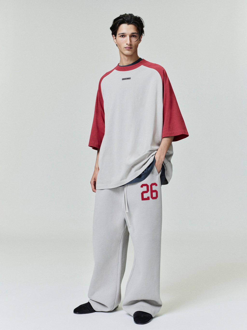 Full body of model wearing loose gray lounge sweatpants with red number 26 on left leg and oversized two-tone top