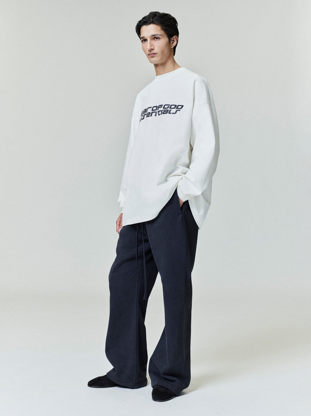 Model standing wearing black Heavy Fleece Flare Sweatpant with wide legs and drawstring, paired with white graphic sweatshirt, gallery 0