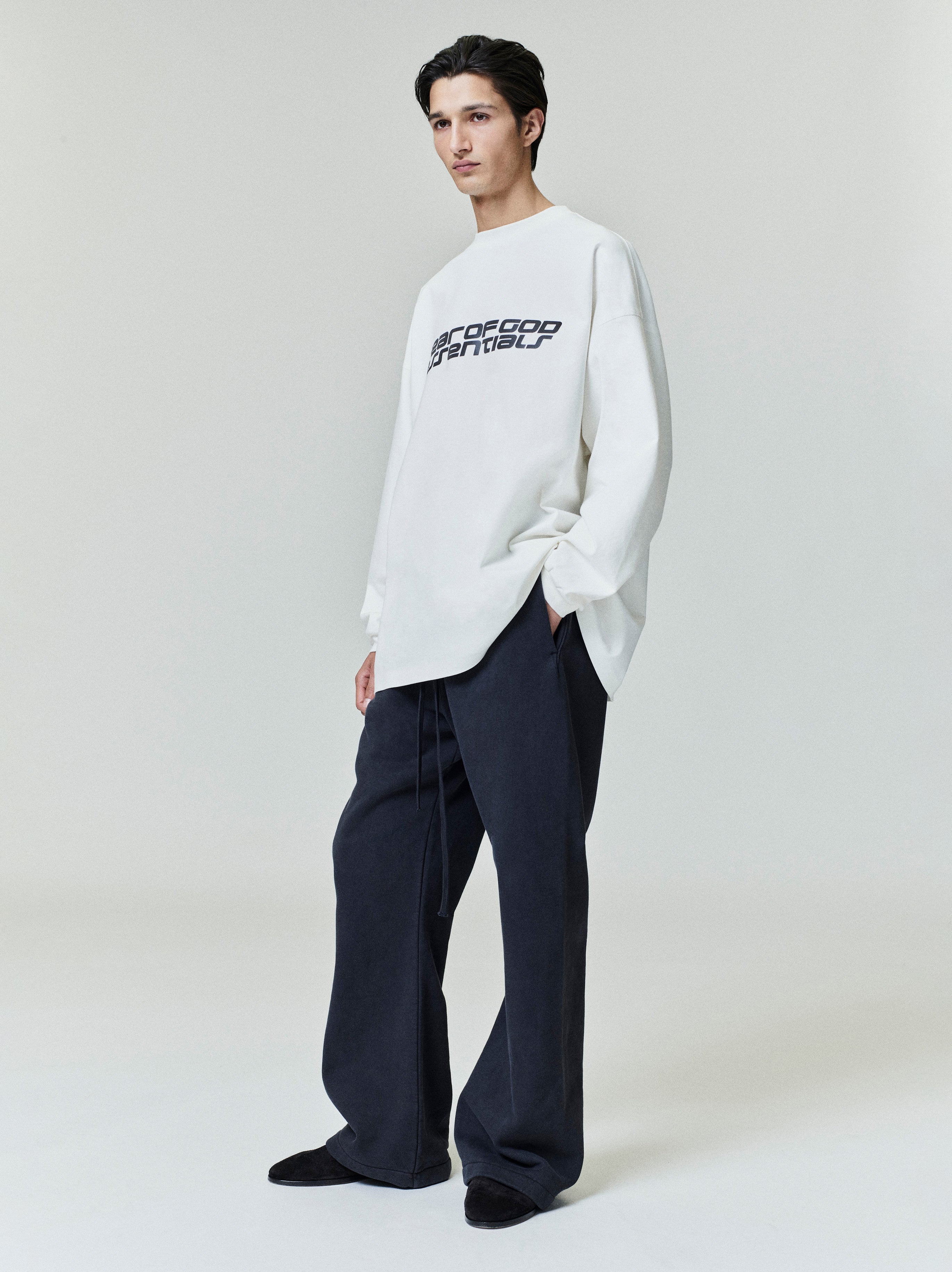 Model standing wearing black Heavy Fleece Flare Sweatpant with wide legs and drawstring, paired with white graphic sweatshirt, gallery 0