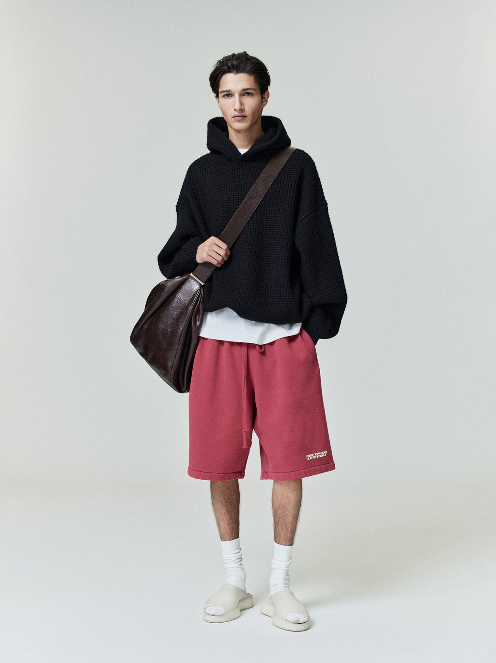 Full body photo of model wearing black Heavy Waffle 90s Hoodie with oversized fit and brown leather shoulder bag