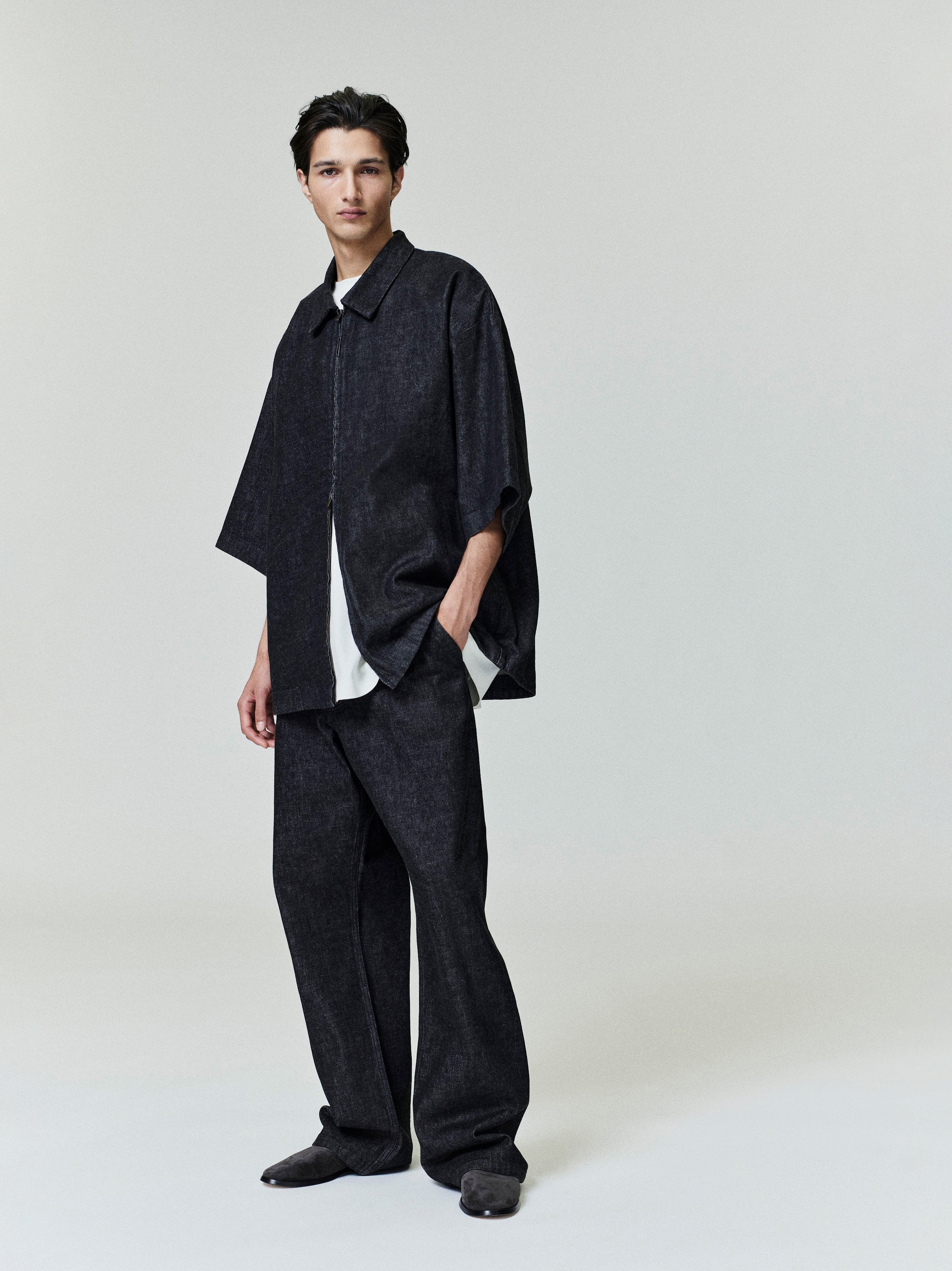 Full-length shot of model wearing black denim work pant and matching oversized half-sleeve shirt on neutral background