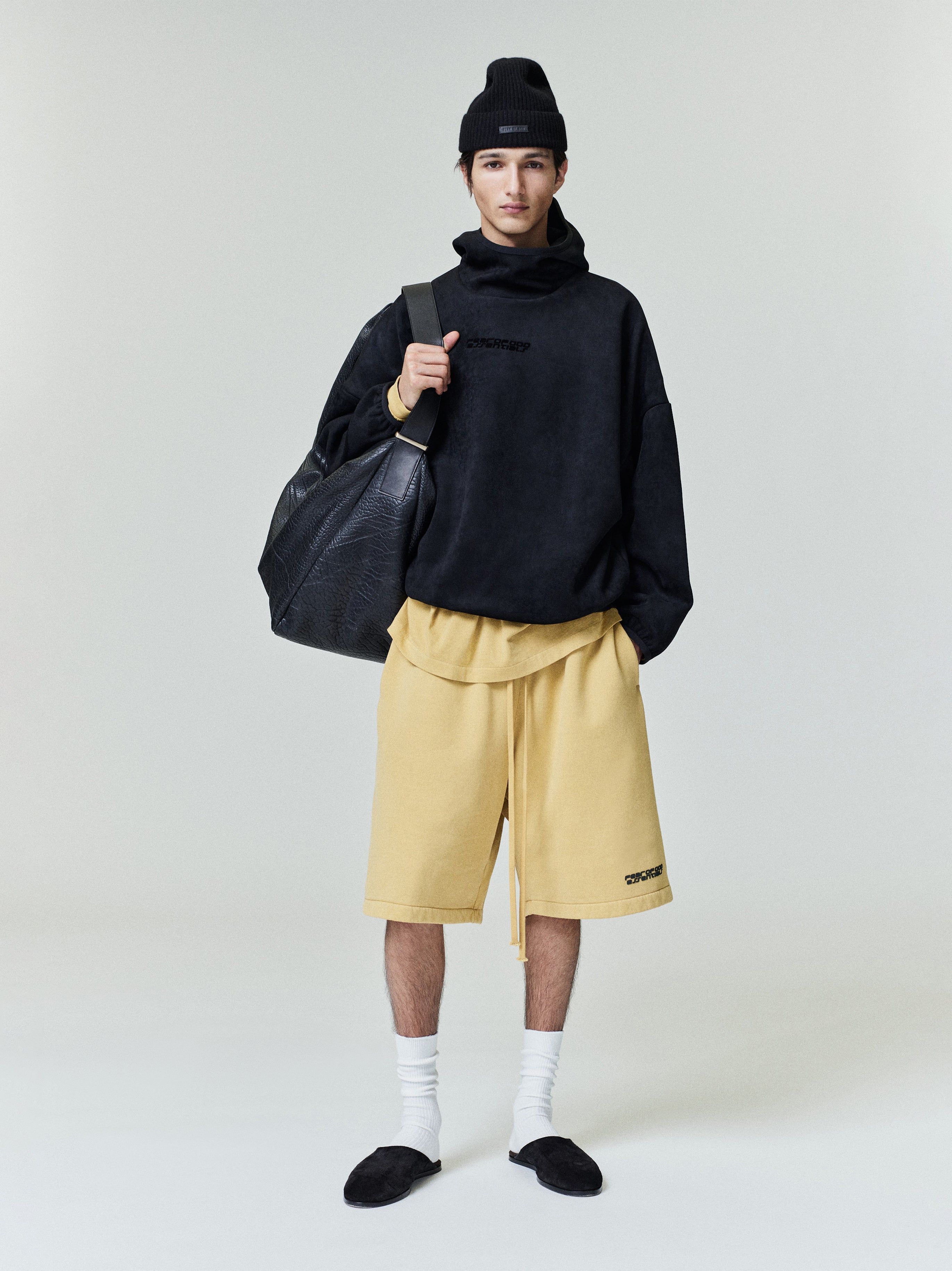 Full body front view of model wearing relaxed sweatshorts in pale yellow with extended drawstrings and logo patch on left leg