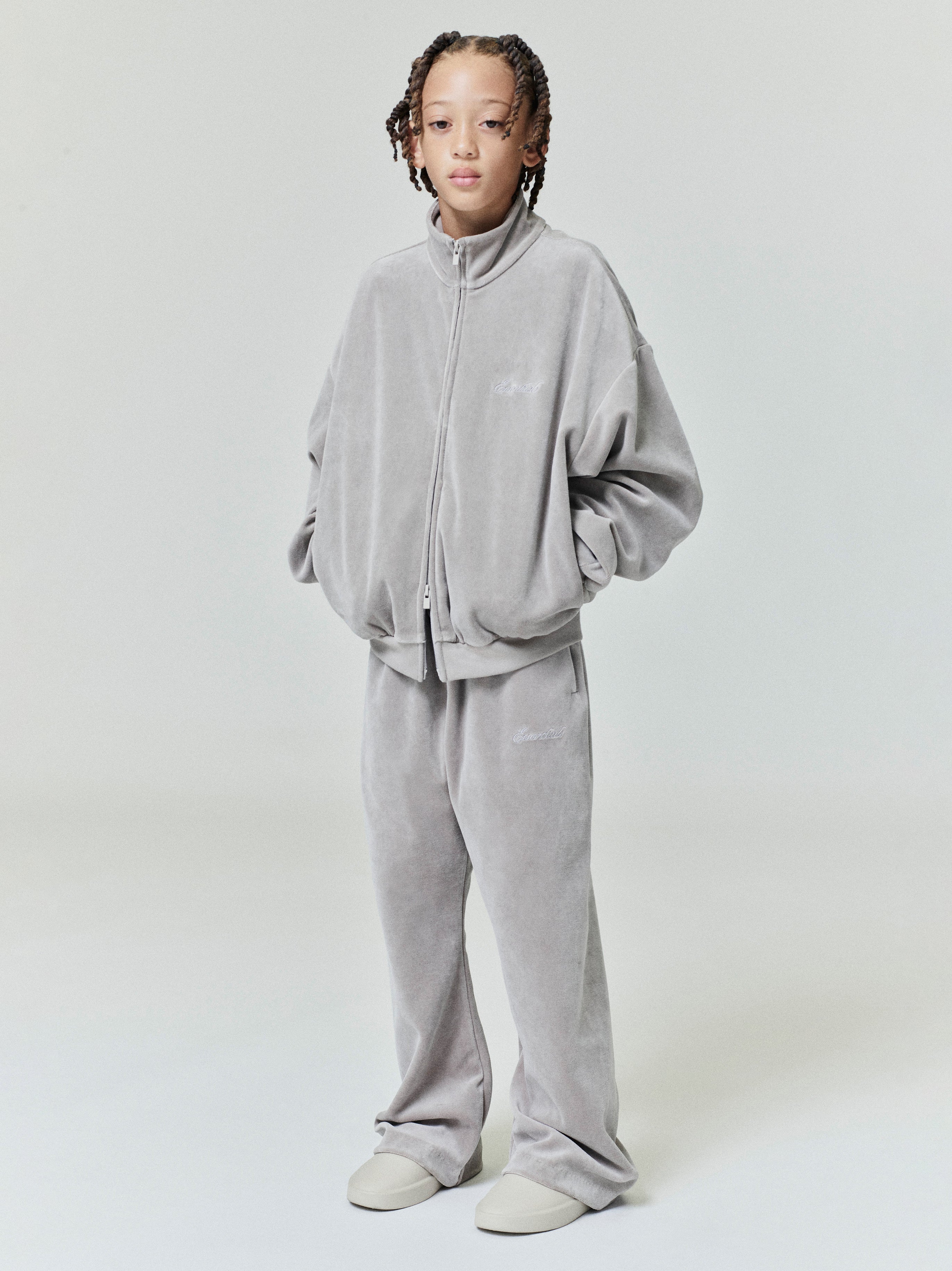 Child wearing a light gray velour zip-up jacket and matching flare sweatpants standing with hands in pockets