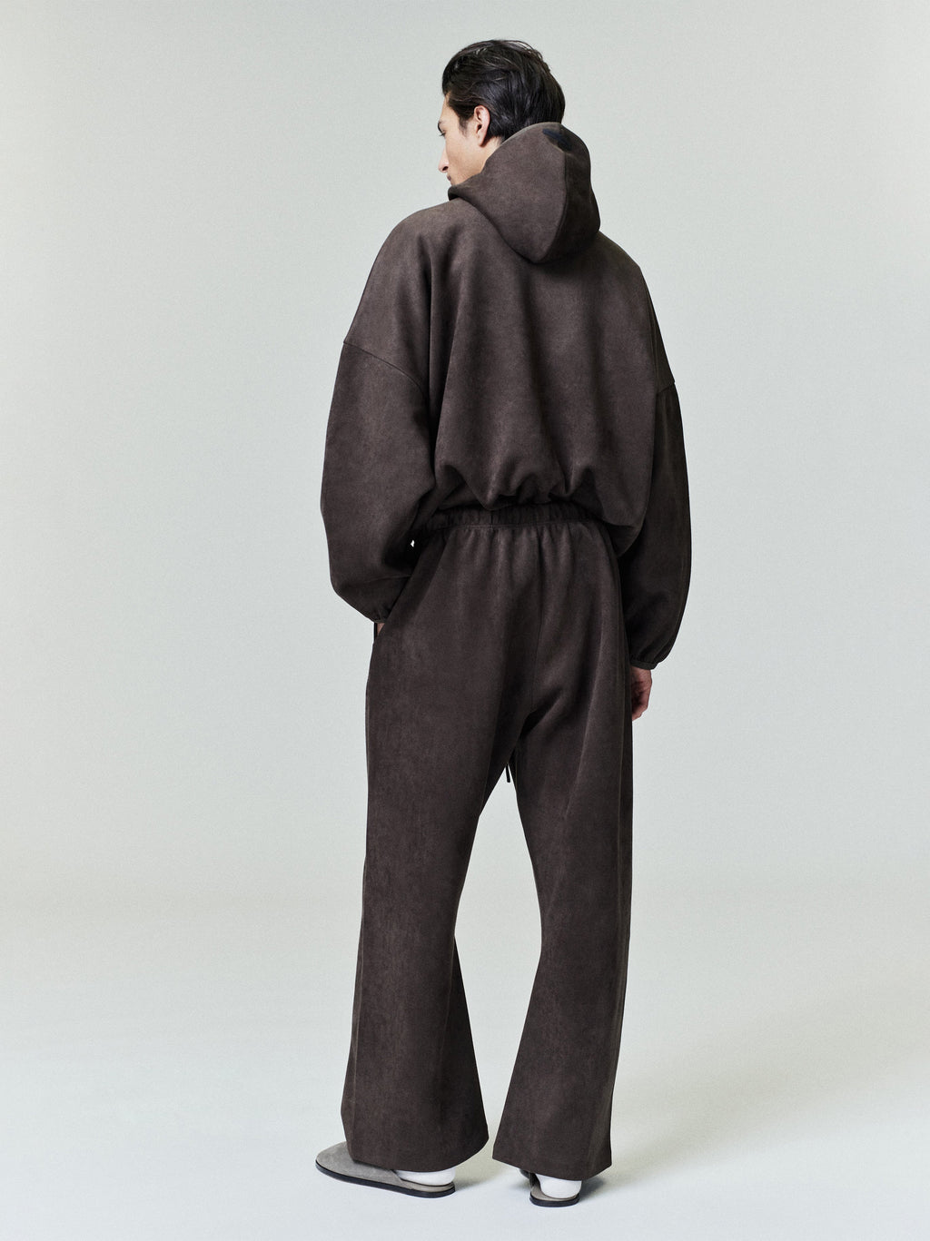 Back view of model wearing dark brown Suede Fleece Flare Pant with elastic waistband and relaxed fit on neutral background