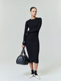 Woman in black ribbed long sleeve midi dress holding black leather bag against gray background