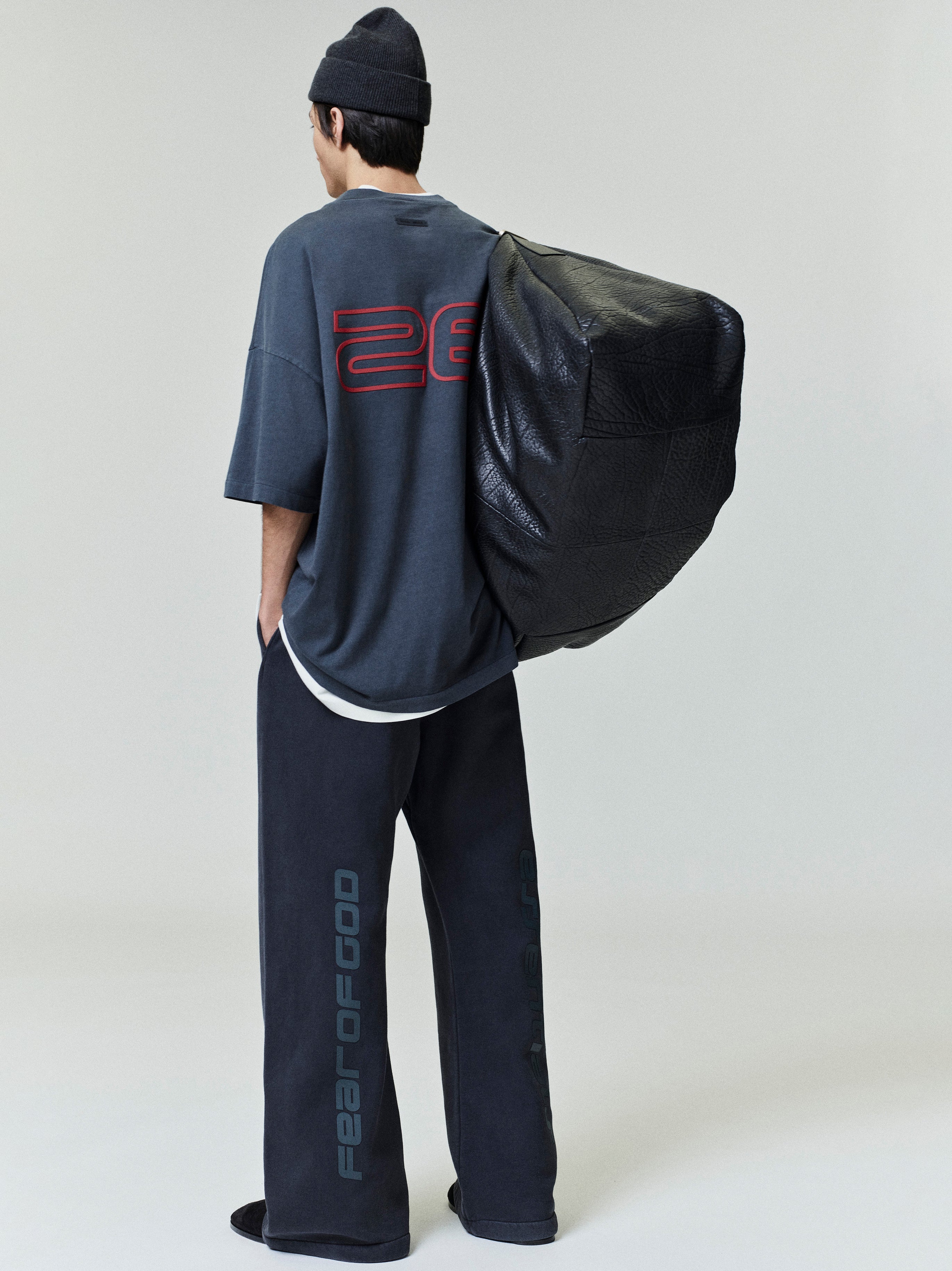 Rear view of model wearing iron grey Fear of God Essentials 90s Tee with red numeric print and relaxed fit, gallery first image