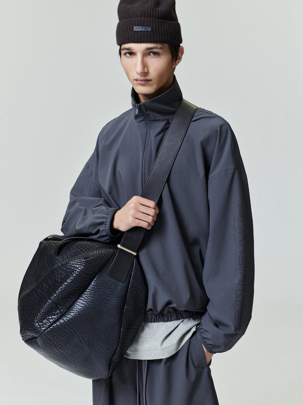 Model wearing charcoal Tech Nylon Half Zip Track Jacket and coordinating pants holding large black textured bag, gallery 0