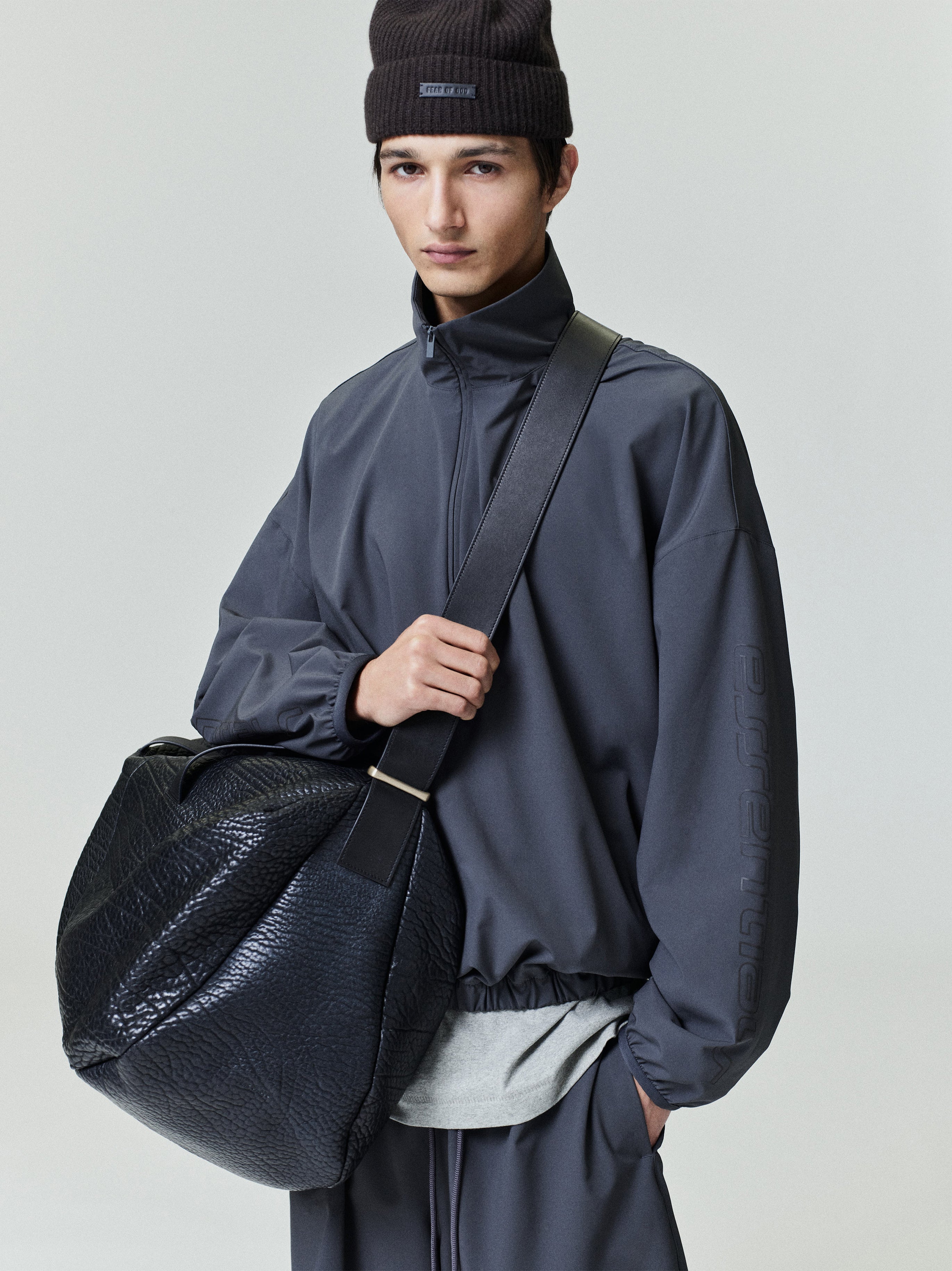 Model wearing charcoal Tech Nylon Half Zip Track Jacket and coordinating pants holding large black textured bag, gallery 0