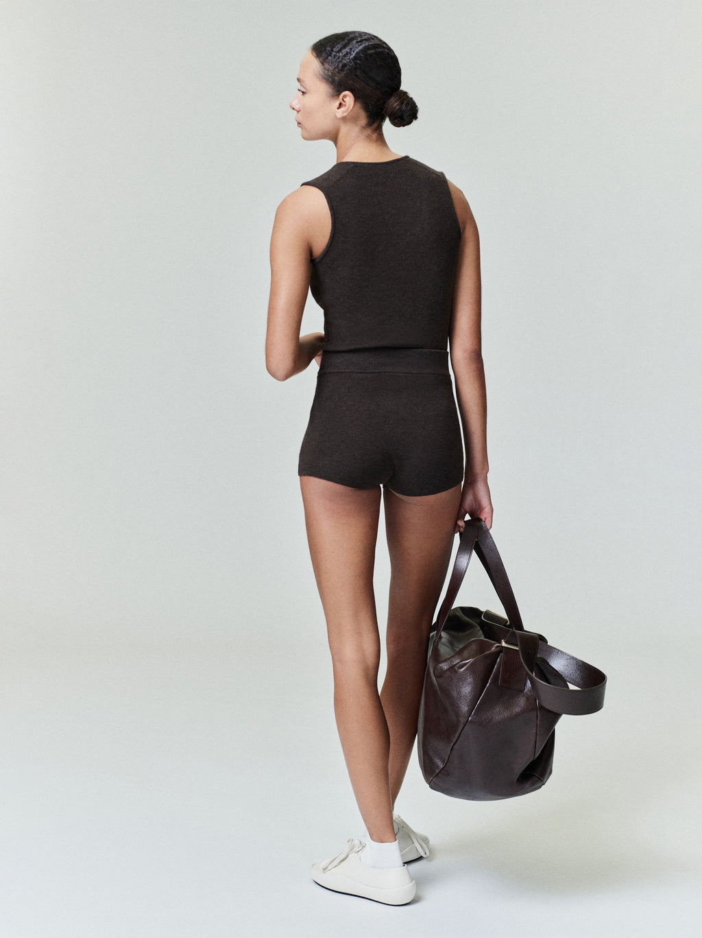 Rear view of woman wearing dark brown ribbed boy shorts and cropped tank holding large brown leather bag 0031_HO25_FW_L08_0934copy.jpg