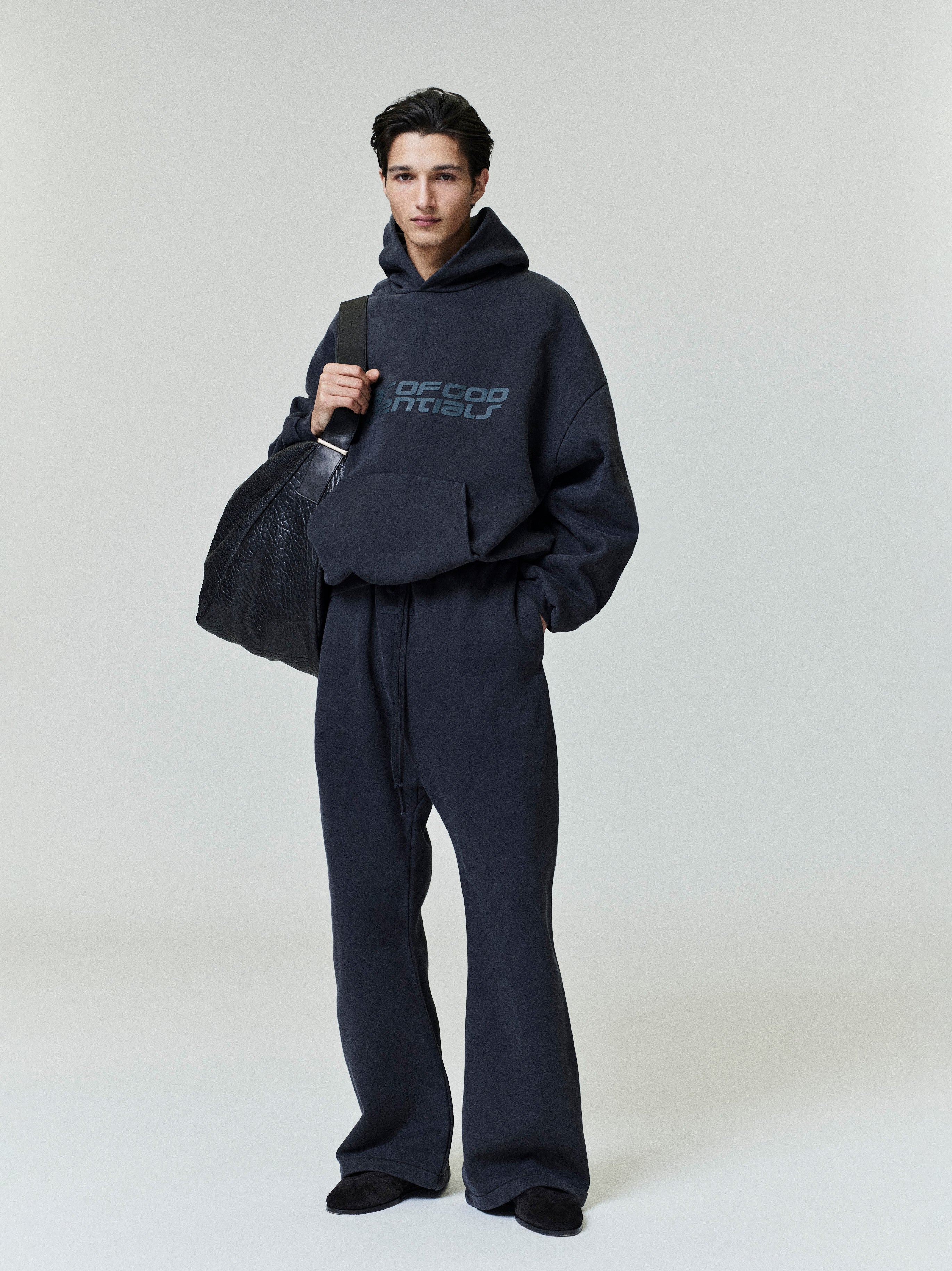 Model wearing dark navy Heavy Fleece 90s Hoodie with matching pants and carrying large black textured bag gallery 0