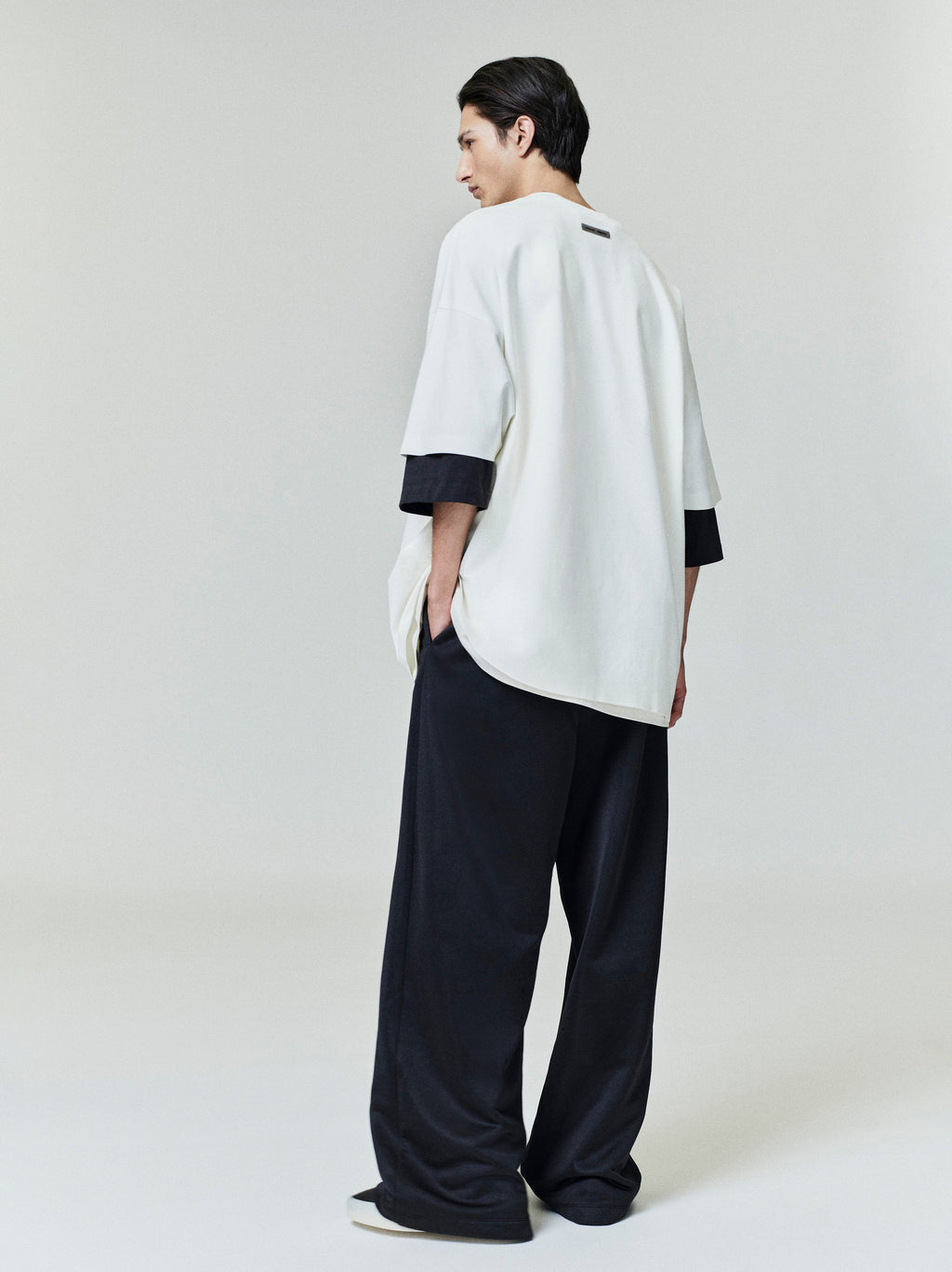 Male model showing back of off-white Ponte 90s Tee with rounded hem and black undershirt sleeves visible, gallery 0034_HO25_F_L38_P08_0606copy.jpg
