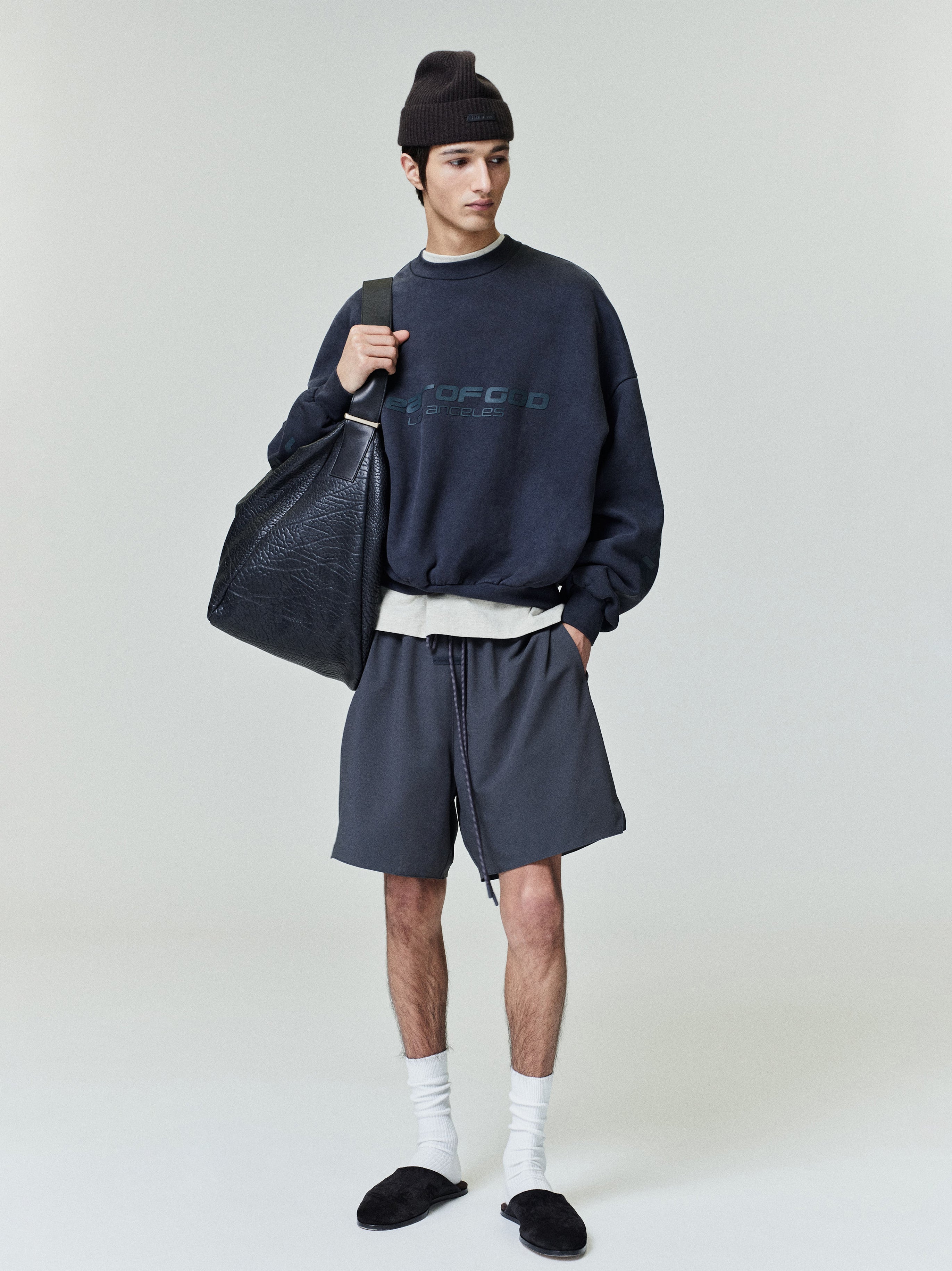 Full-length front view of model wearing navy Los Angeles heavy fleece cropped sweatshirt with black beanie and large leather bag