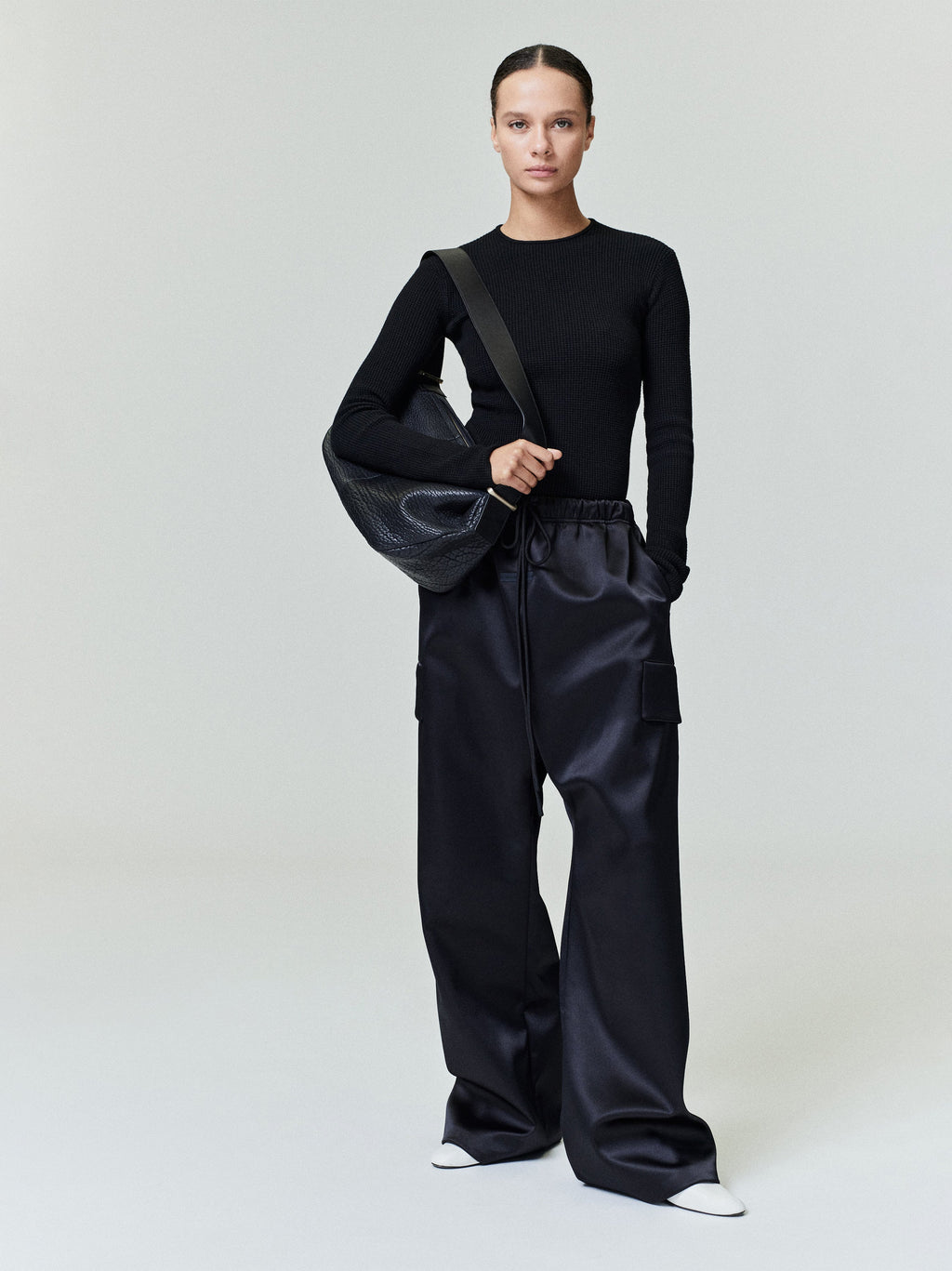 Model facing front wearing black Bonded Satin Field Pant with cargo pockets and elastic waistband, gallery 0, file 0037_HO25_FW.jpg