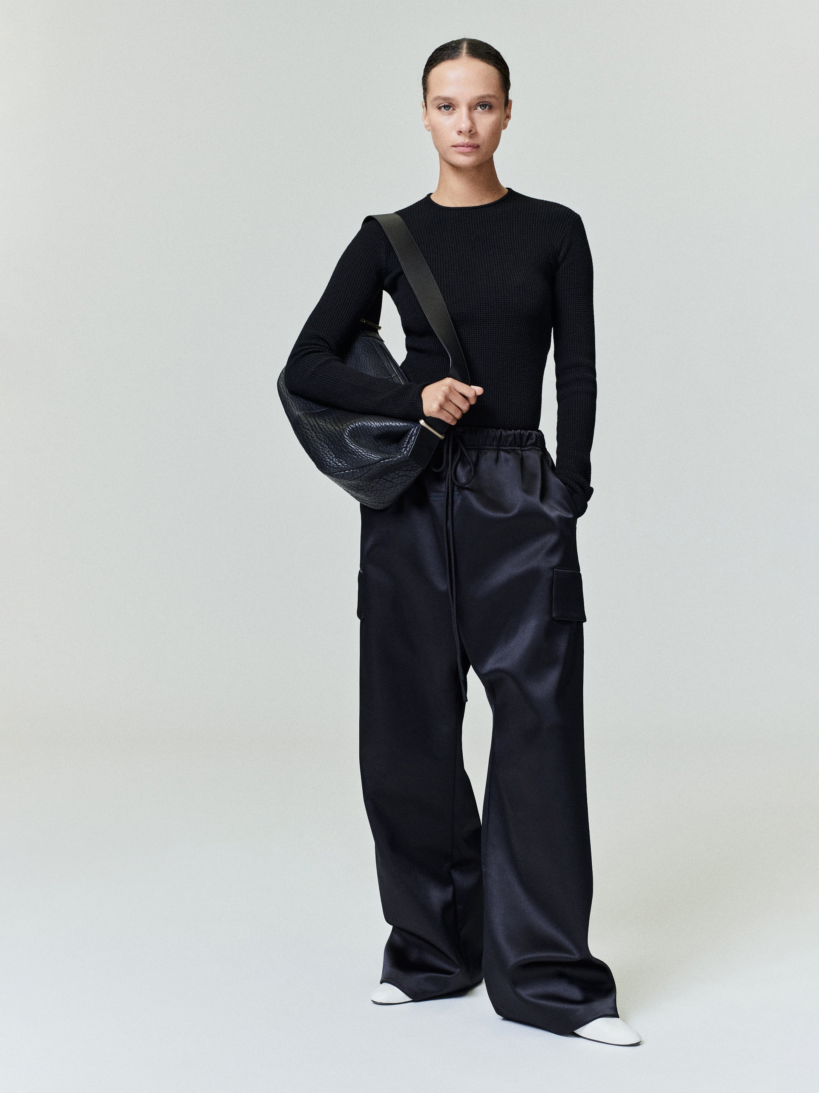 Model facing front wearing black Bonded Satin Field Pant with cargo pockets and elastic waistband, gallery 0, file 0037_HO25_FW.jpg