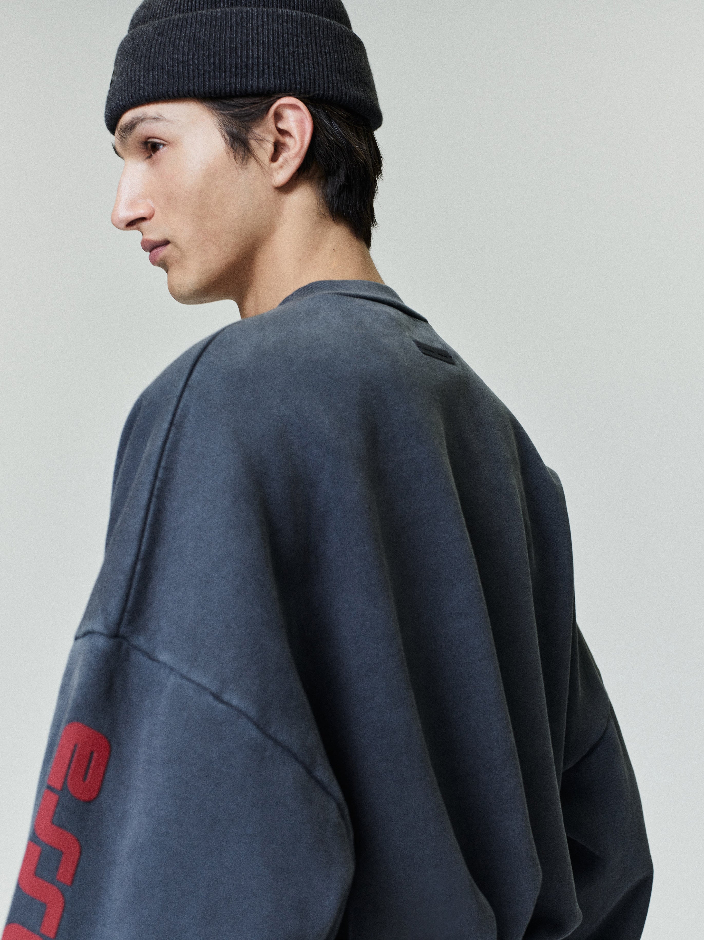 Rear view of model wearing faded navy Chicago heavy fleece cropped sweatshirt with red sleeve lettering and black knit beanie
