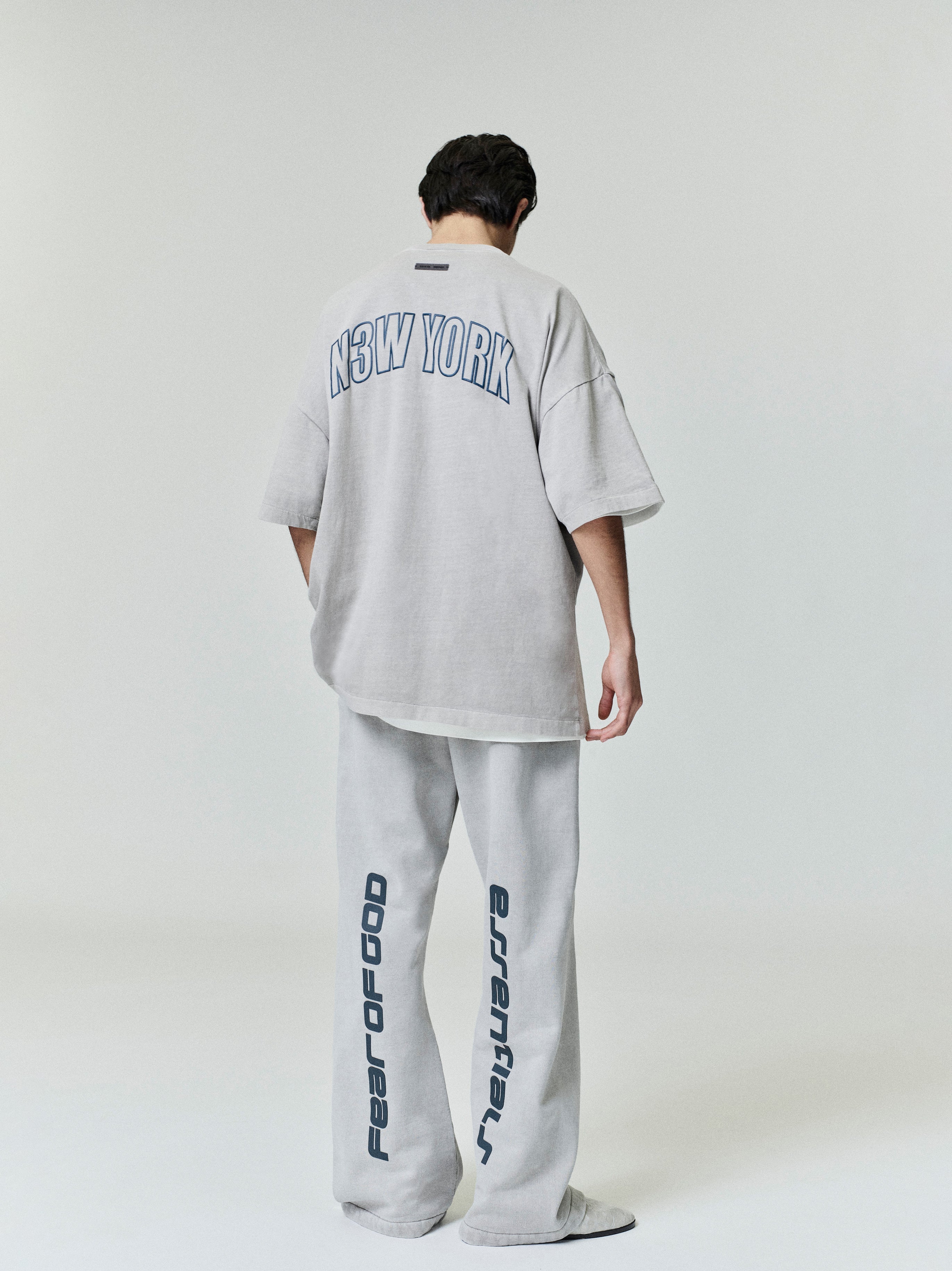 Model showing back of oversized light grey New York 90s Tee with navy print, paired with matching wide sweatpants in first gallery image