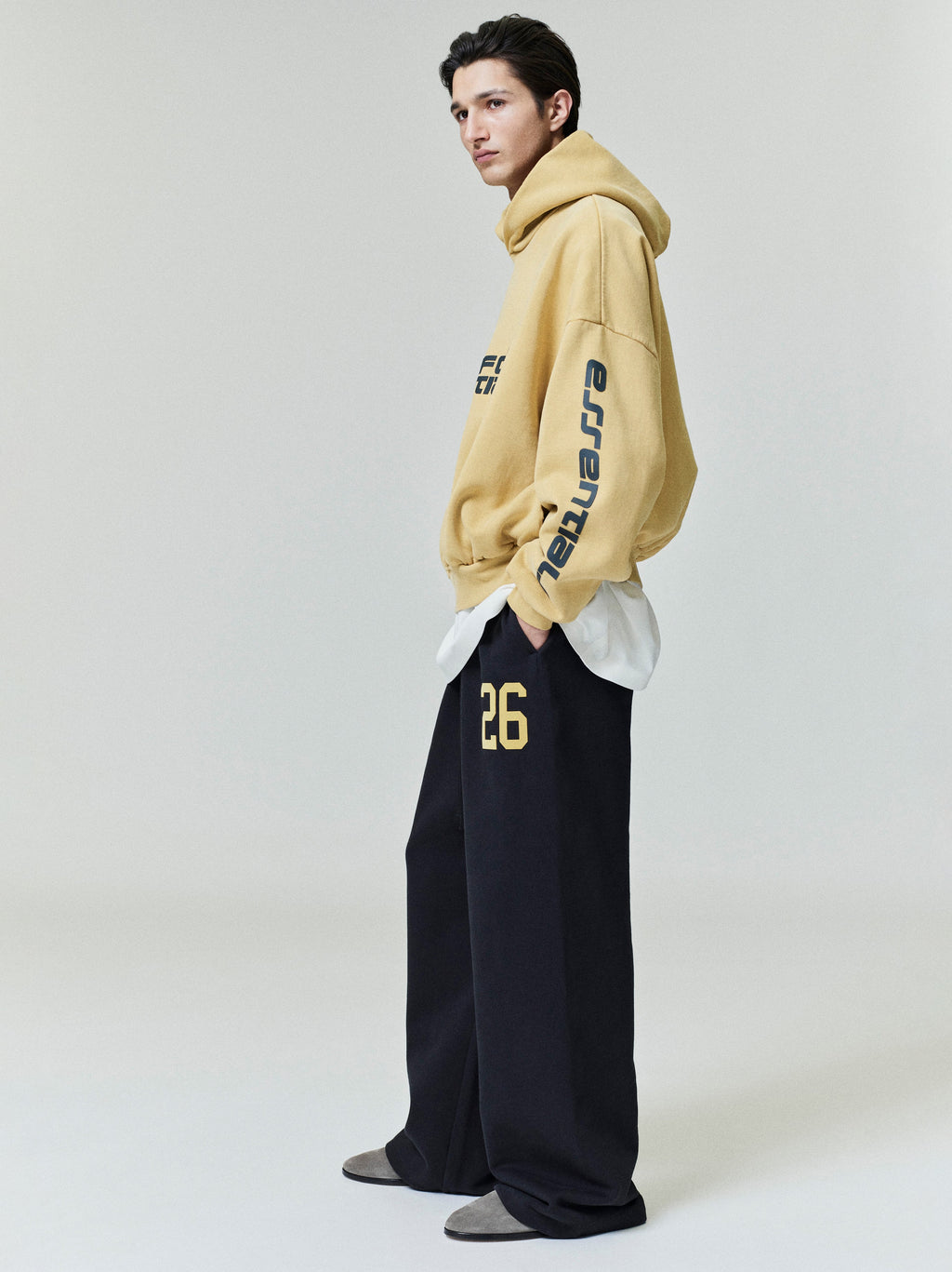 Male model wearing black Lounge Sweatpant with yellow "26" print and oversized tan hoodie, side profile, gallery image 0