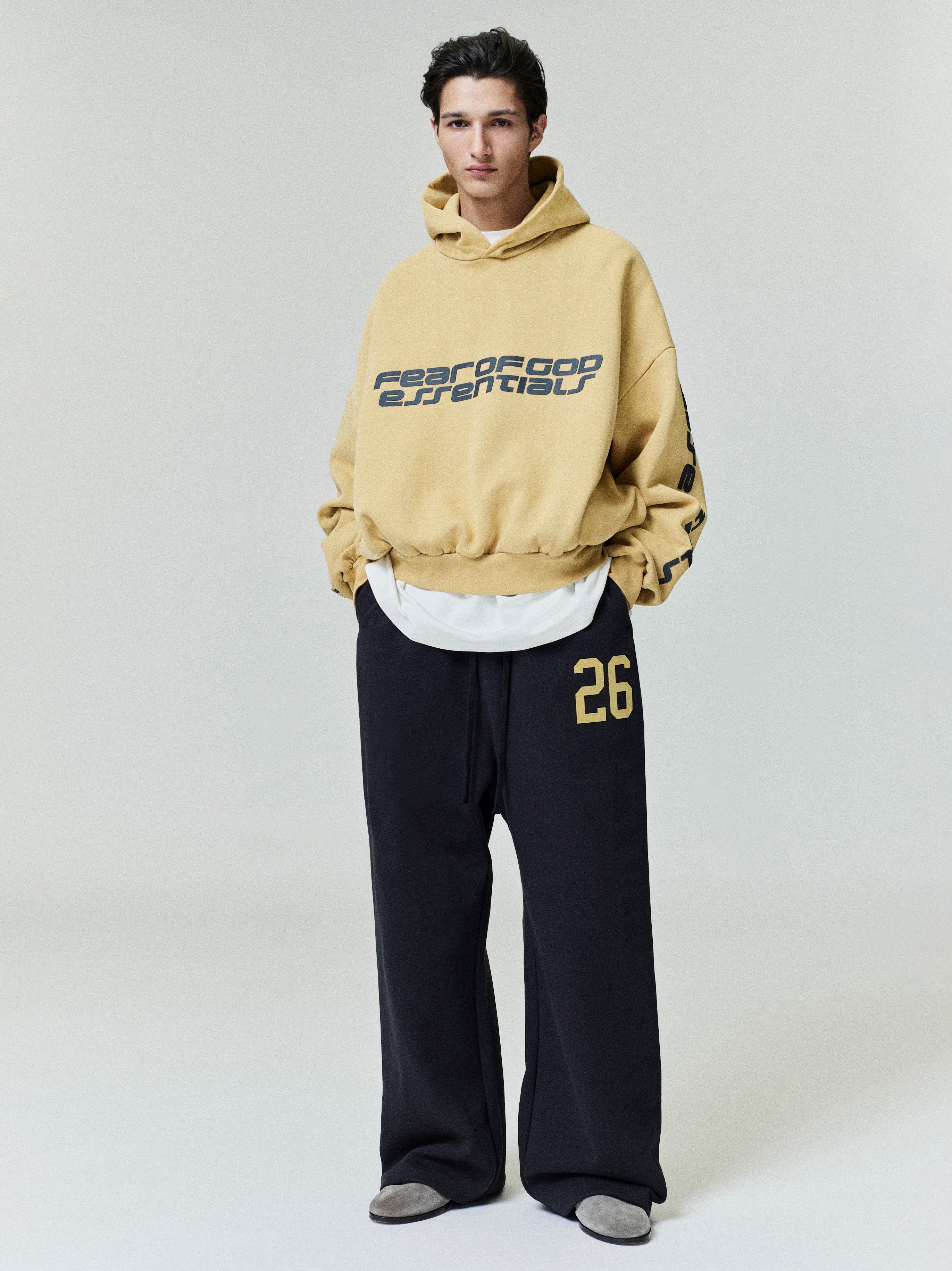 Male model wearing black Lounge Sweatpant with yellow "26" detail and oversized tan hoodie with graphic text, front view