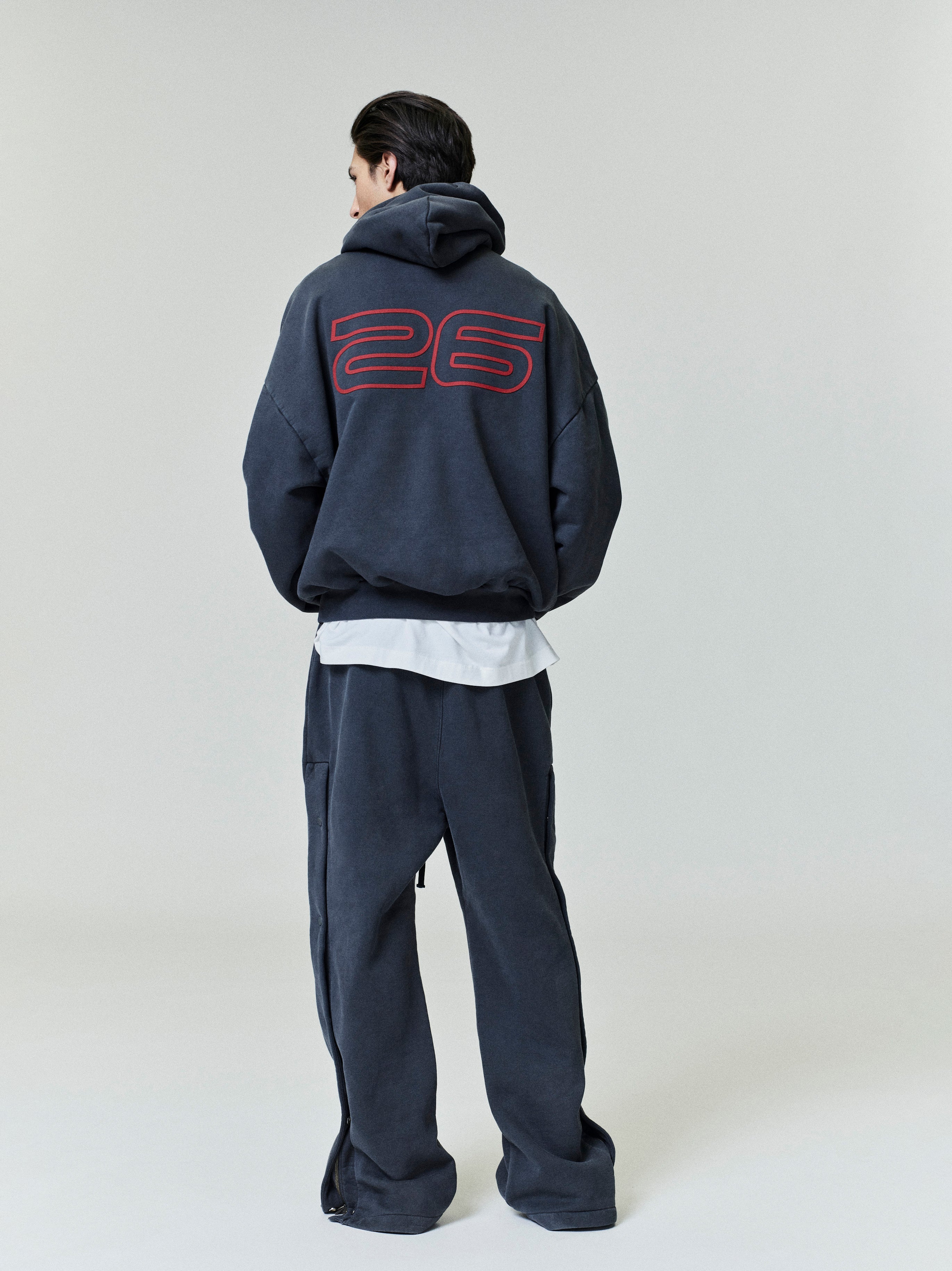 Person wearing a dark grey tracksuit with a large red '26' on the back against a white background
