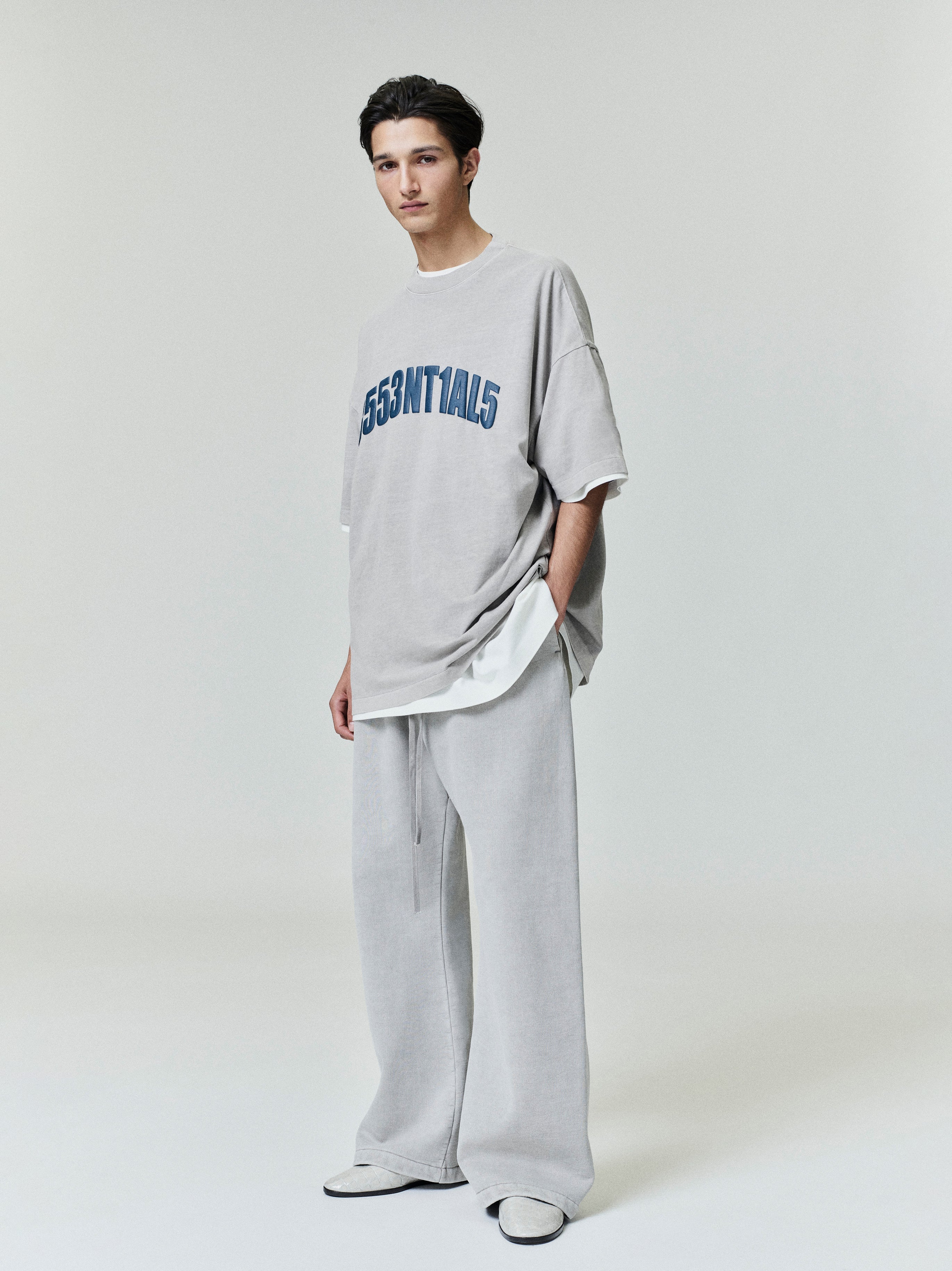 Standing model wearing light grey New York 90s Tee with navy alphanumeric print and matching relaxed wide-leg pants