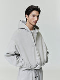 Side angle of light grey Embroidered Classic Full Zip Hoodie with oversized fit and model’s hands in pockets on neutral background