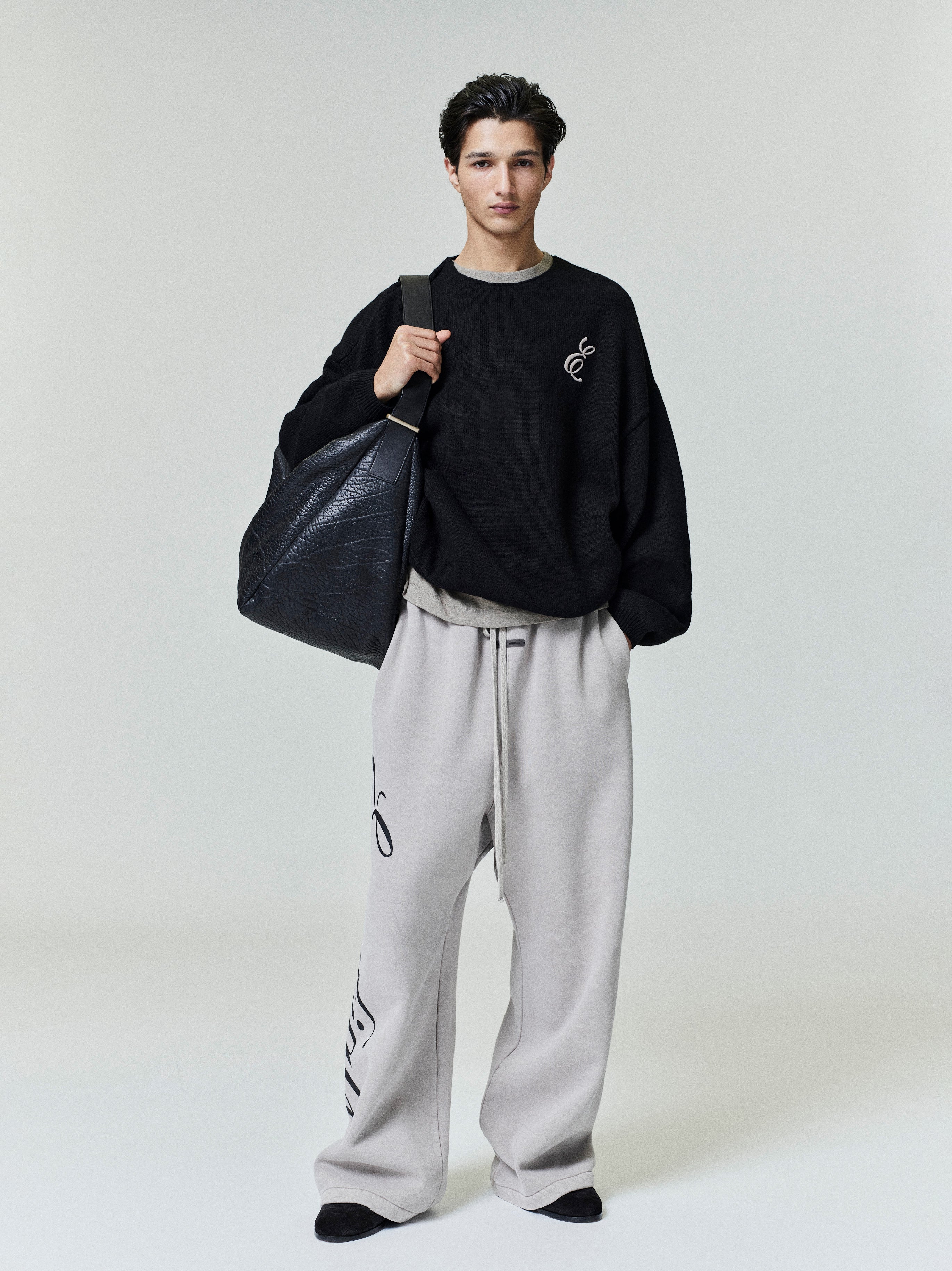 Model wearing light gray Heavy Fleece Lounge Sweatpant with side script detail, paired with black sweatshirt and large black bag, gallery 0