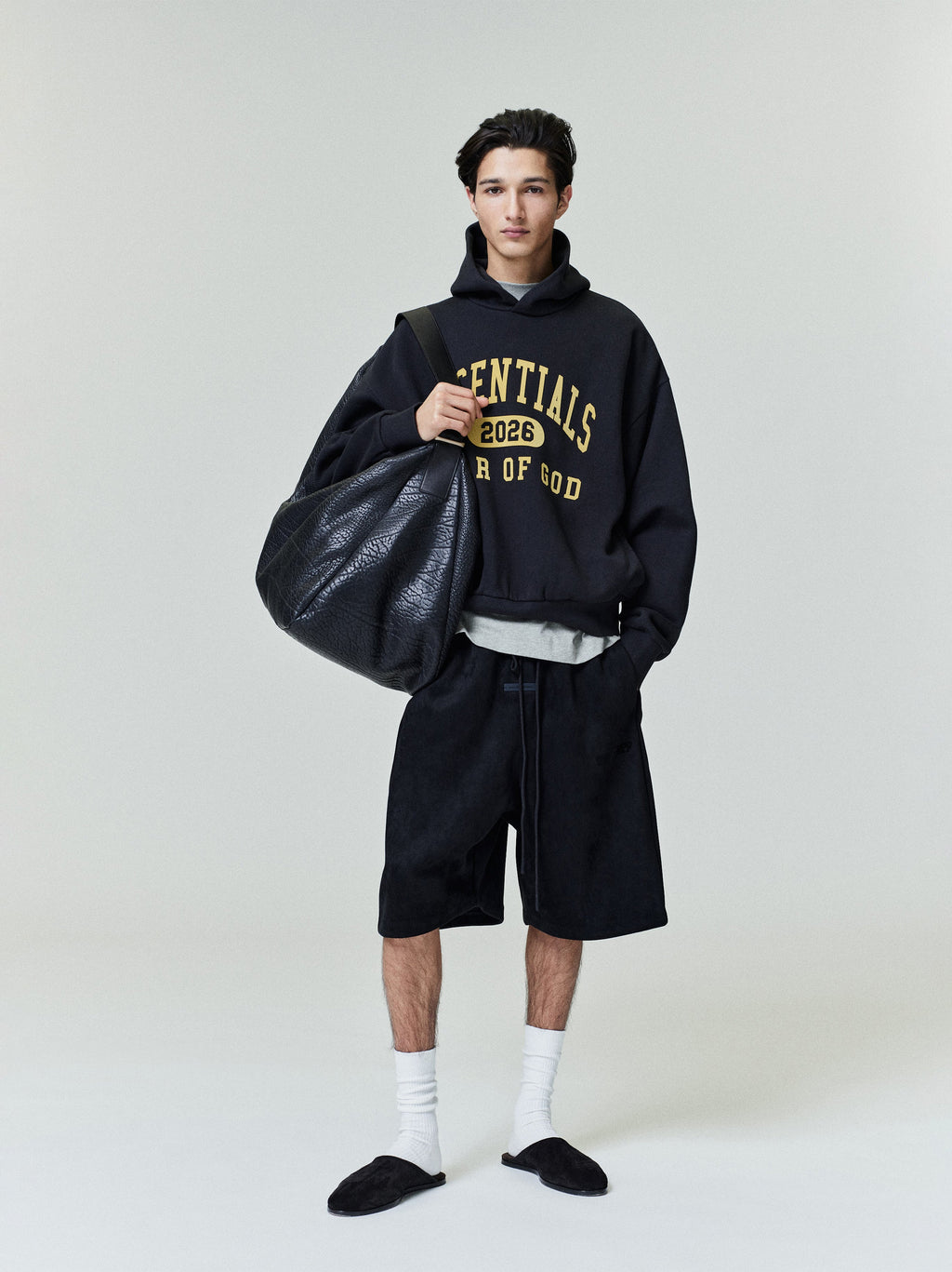 Full front view of model wearing black Classic Fleece Hoodie with yellow Essentials 2026 text and loose black shorts gallery 0