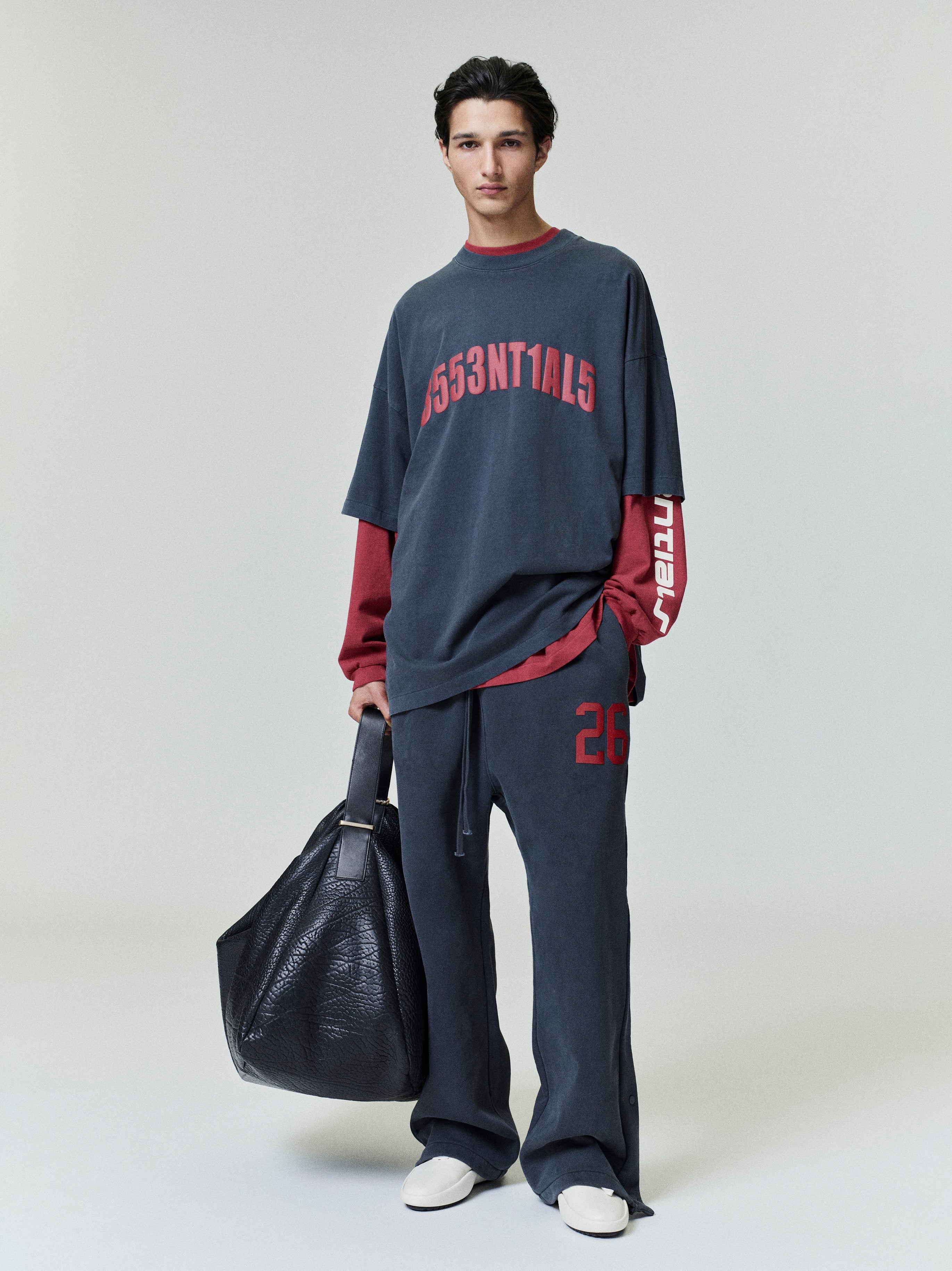 Full-length photo of model wearing dark Chicago 90s Tee layered over red long-sleeve top with matching pants and black leather bag