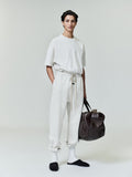 Model standing wearing off-white Classic Sweatpant with extended drawstring and relaxed fit holding dark brown leather duffel bag
