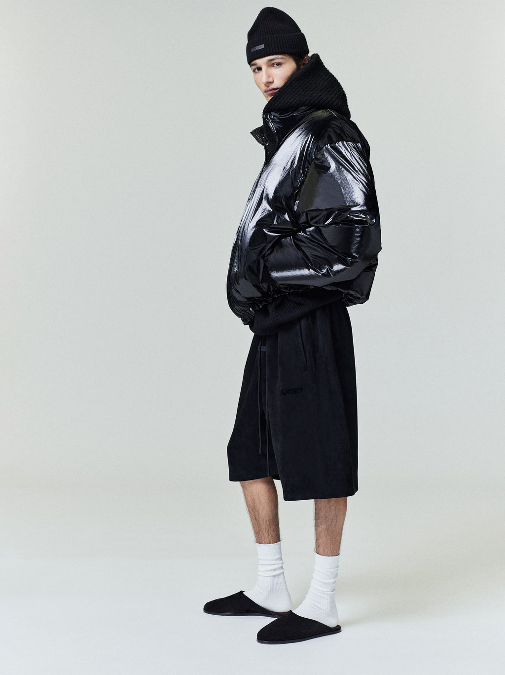 Side view of model wearing glossy black ripstop nylon puffer jacket with high collar and knit beanie, gallery position 0