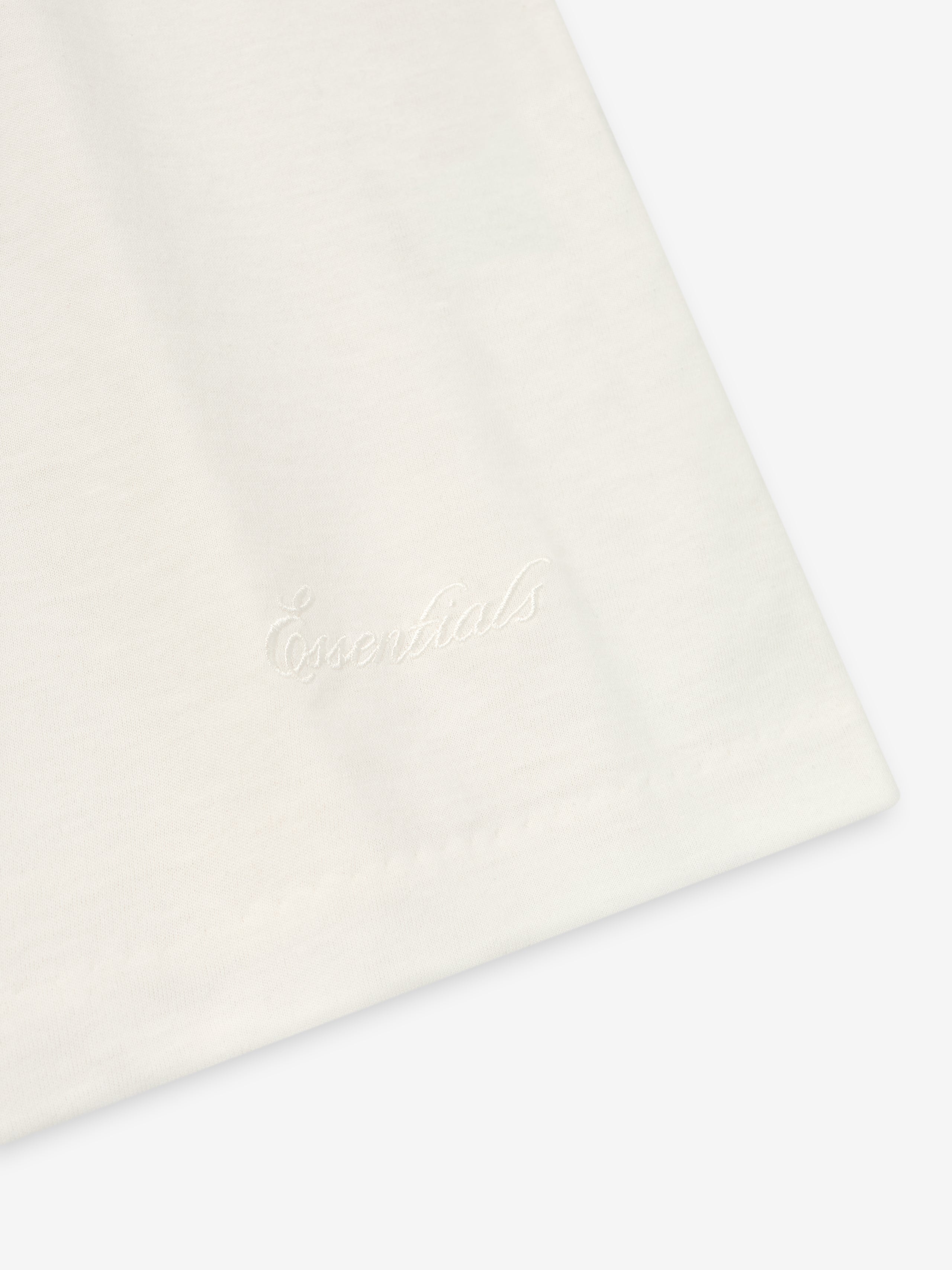 Close-up of ivory Embroidered Essential Tank showing subtle tonal "Essentials" script embroidery near hem, gallery image 0
