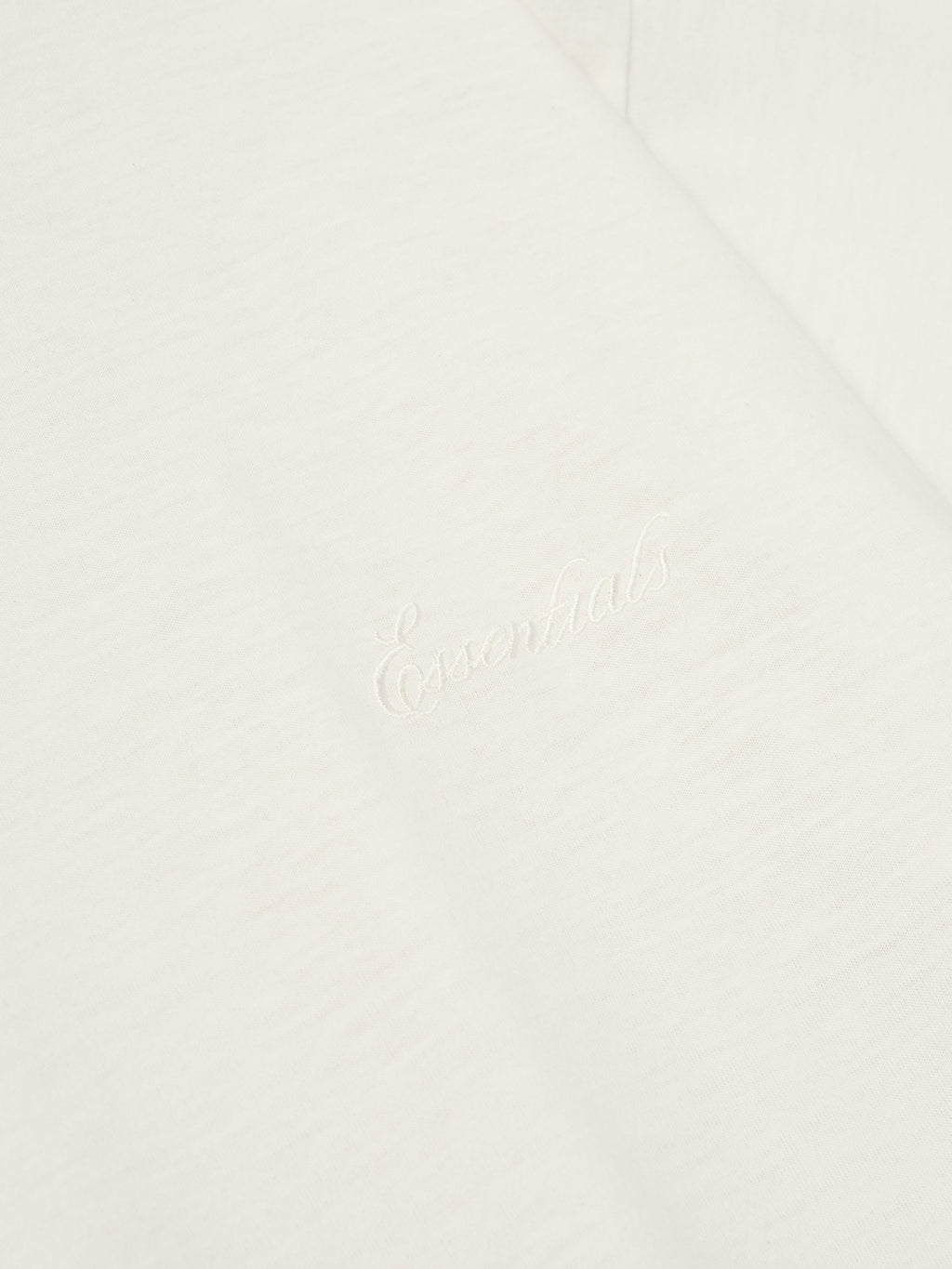 Close-up of ivory Embroidered Essential Tee showing subtle tonal logo detail on soft fabric, gallery image 0