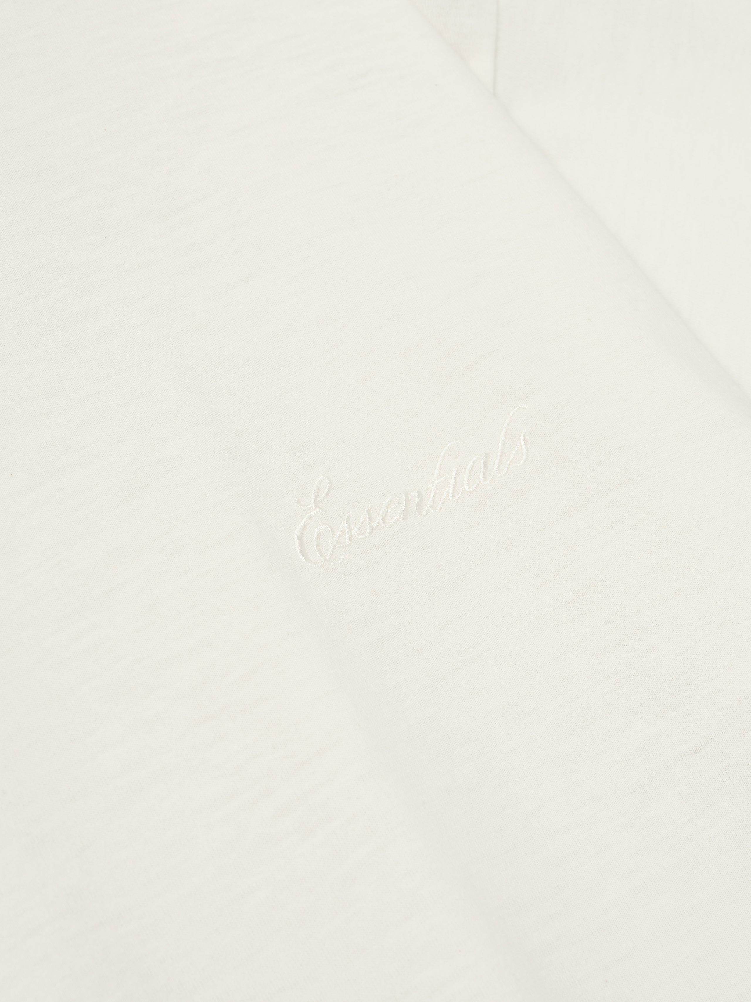 Close-up of ivory Embroidered Essential Tee showing subtle tonal logo detail on soft fabric, gallery image 0