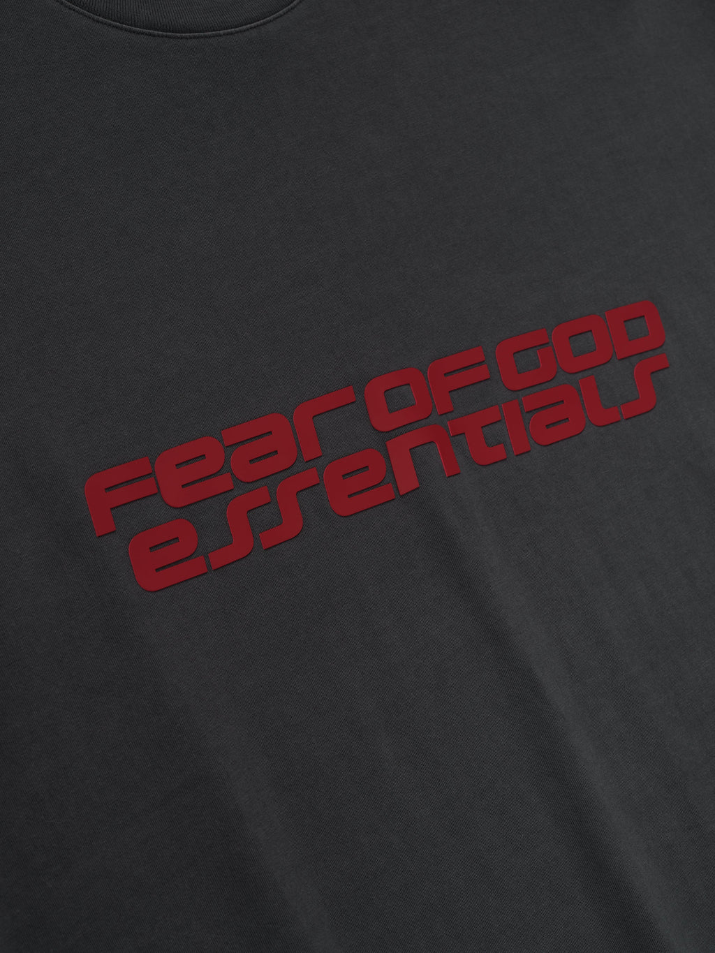 Close-up of iron grey Fear of God Essentials 90s Tee showing bold red logo text on smooth soft fabric front, gallery first image