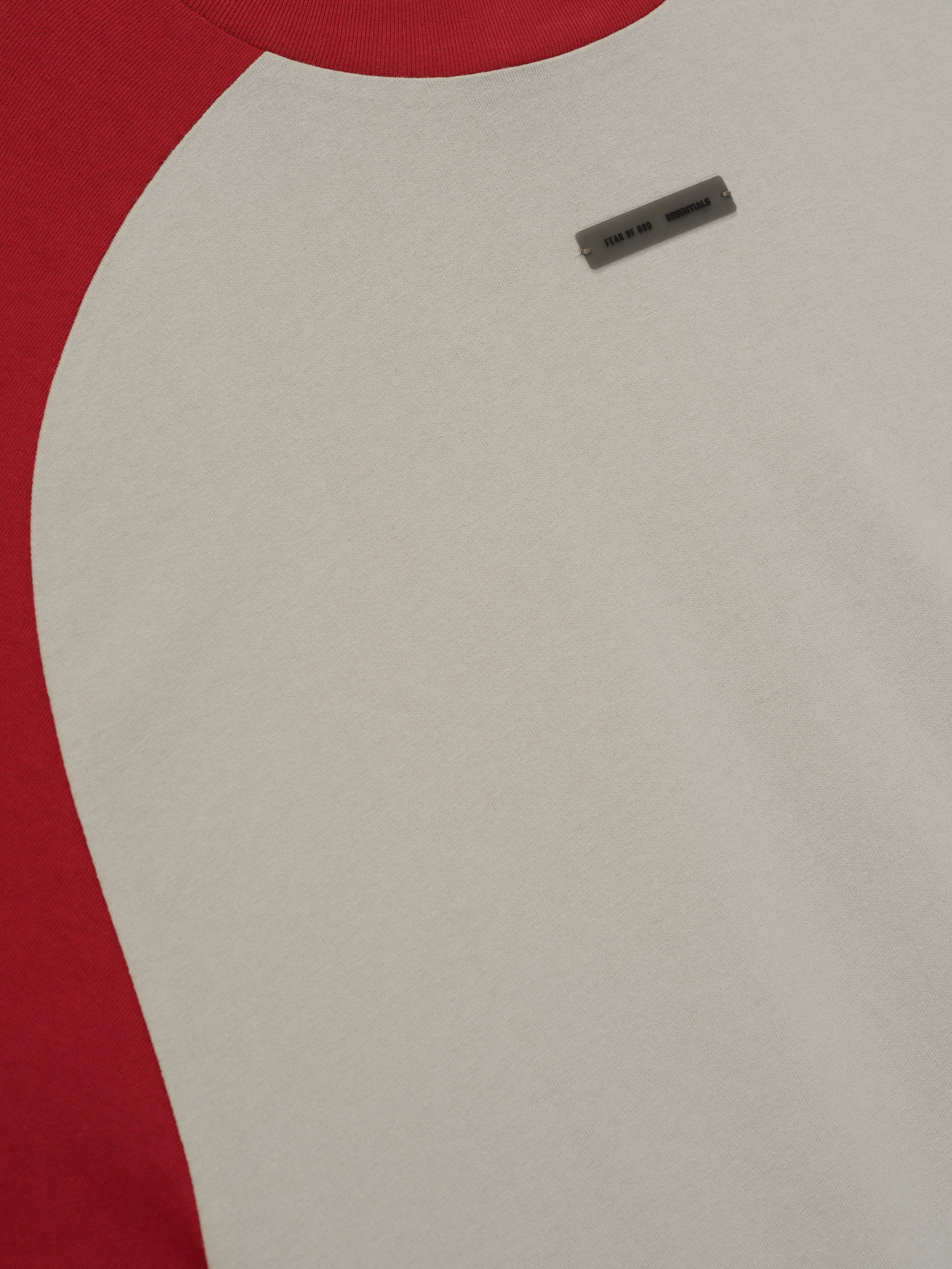 Close-up of smoke grey baseball tee with crimson raglan sleeve and small rectangular label near chest area.