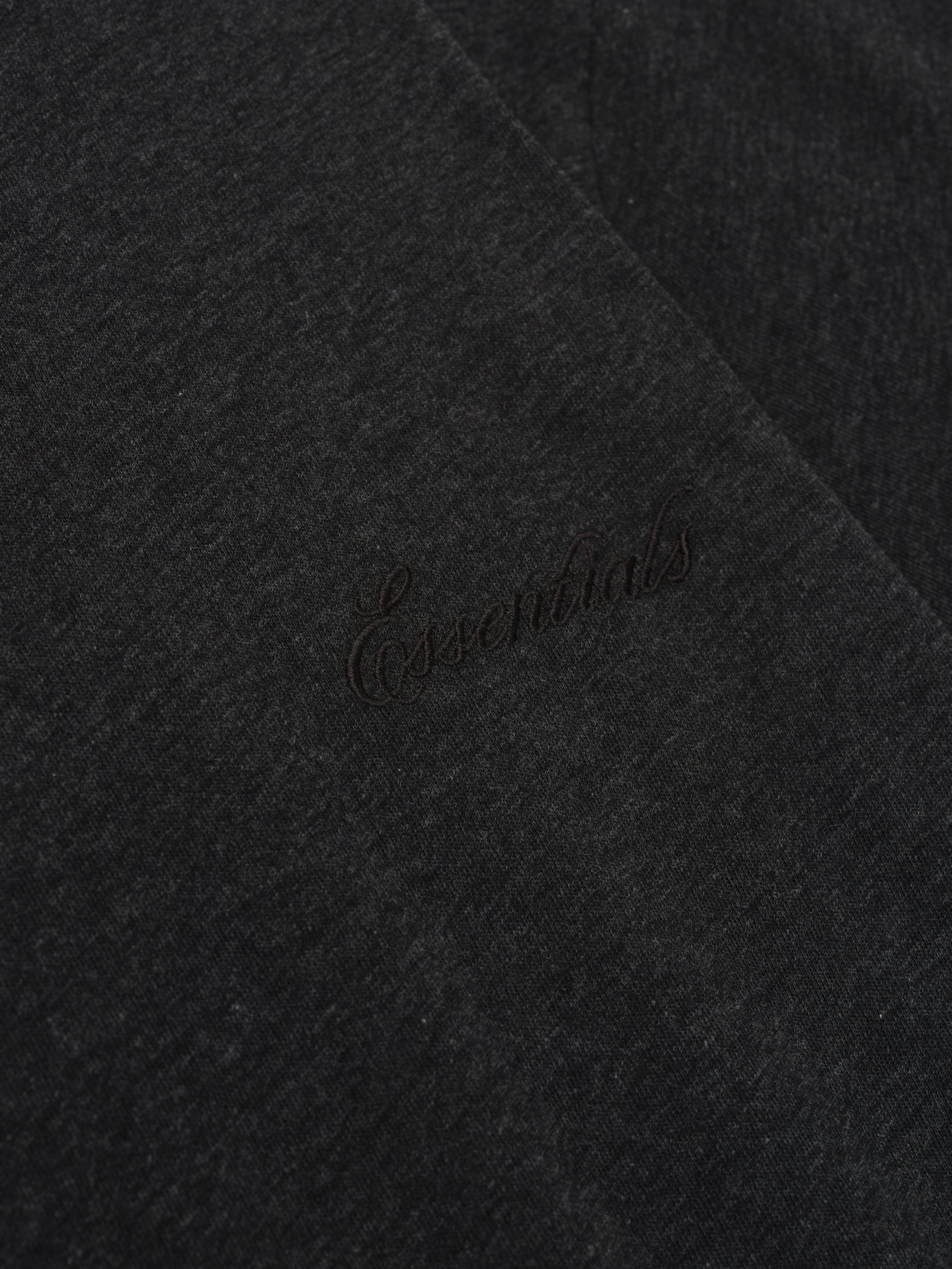 Close-up of vintage black Womens Classic Tee showing subtle tonal "Essentials" embroidery on soft fabric surface