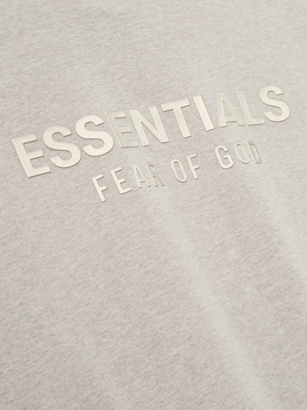 close-up of light beige cotton jersey tee with embossed ESSENTIALS Fear of God logo on chest area